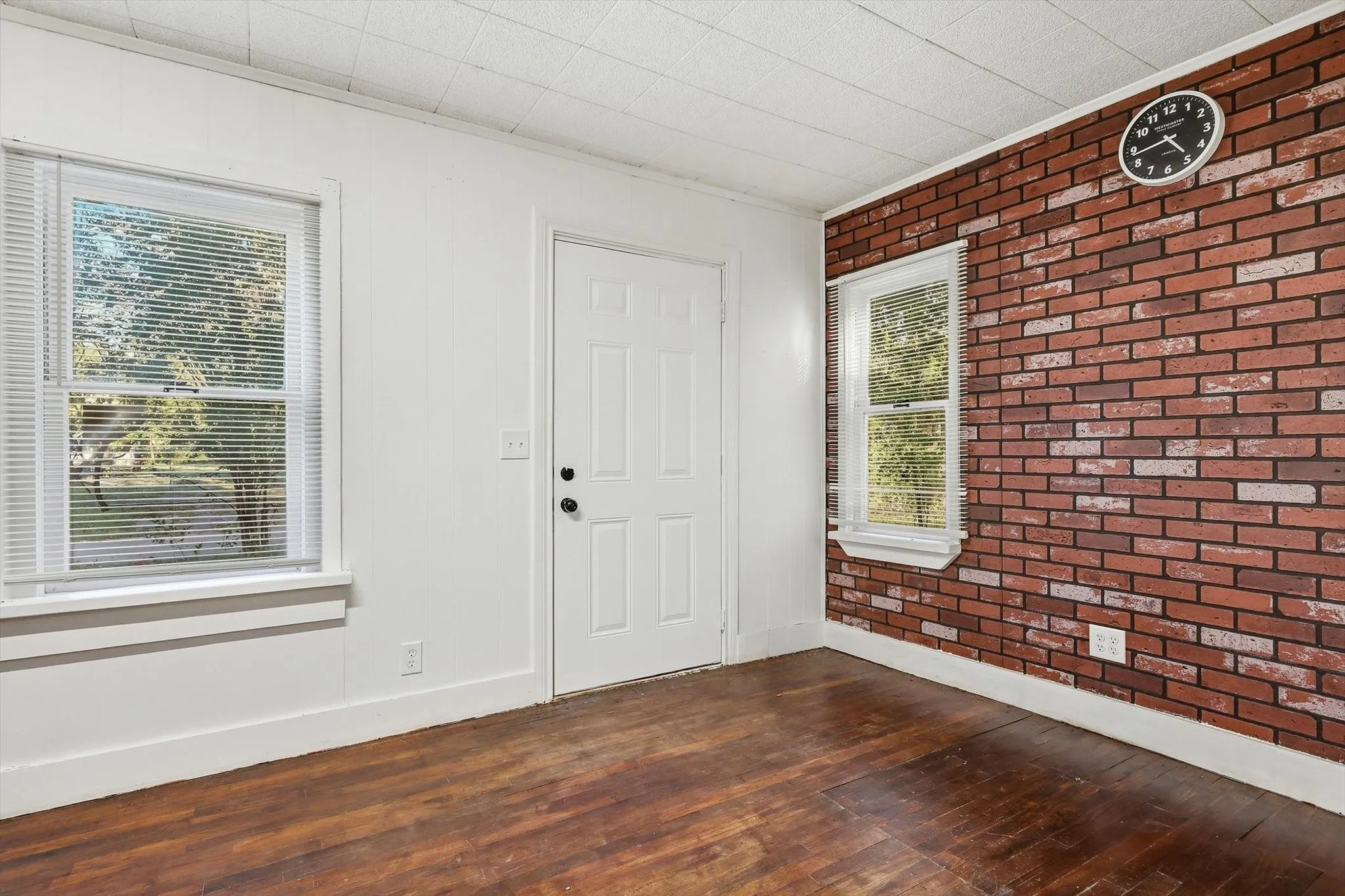 Wood-finish flooring with white trim, a white paneled door, and two windows with blinds