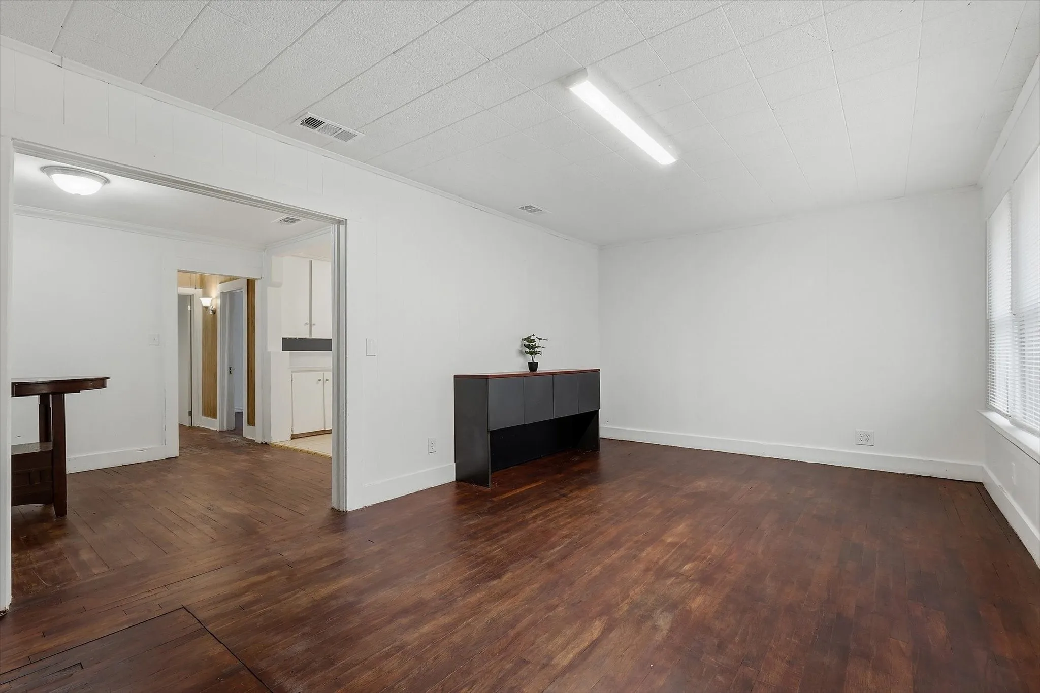 Spacious room featuring wood-finish flooring, white walls, and a dropped ceiling with recessed lighting