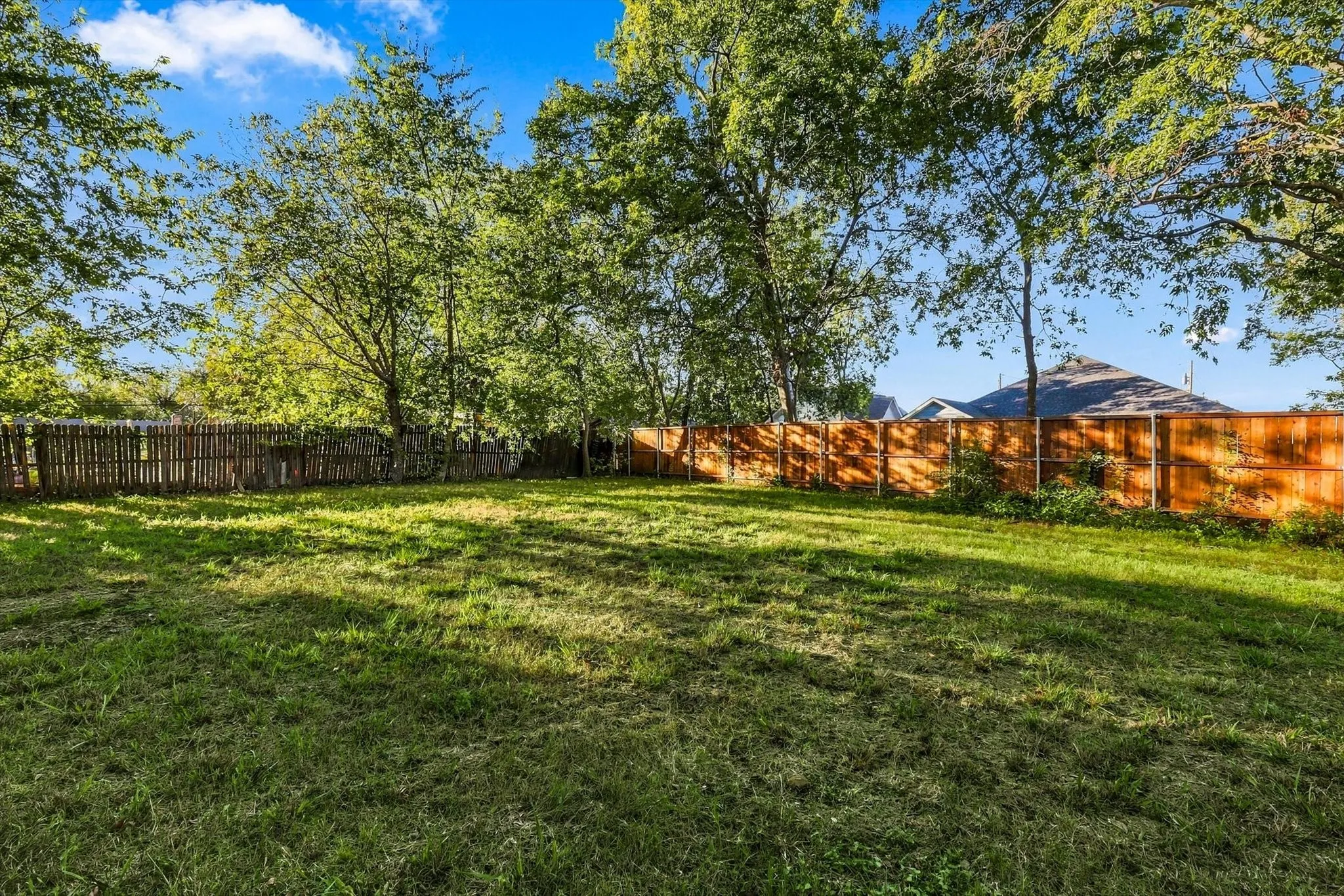 Expansive grassy yard with mature trees and a wood picket fence
