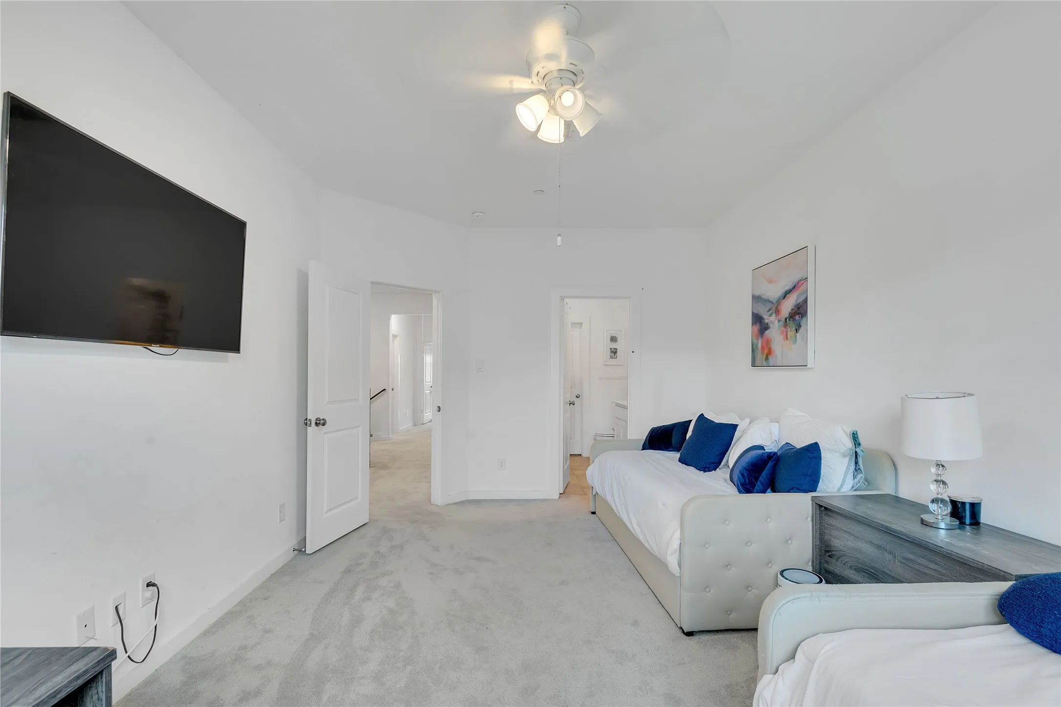 Carpeted room with a ceiling fan, featuring white walls and a wall-mounted display