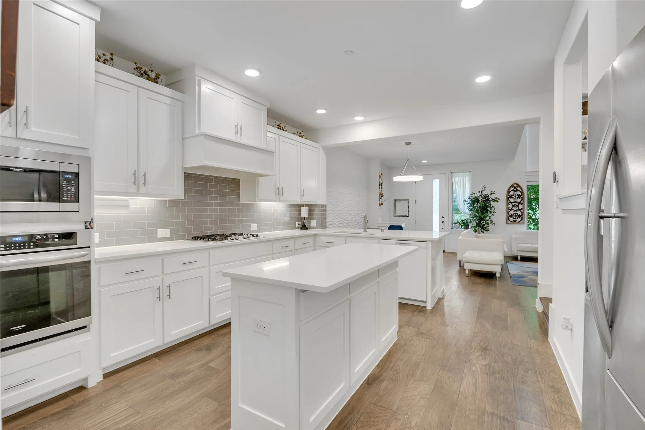 Modern kitchen featuring an island, white cabinetry, integrated stainless steel appliances, a tile backsplash, and wood-finish flooring