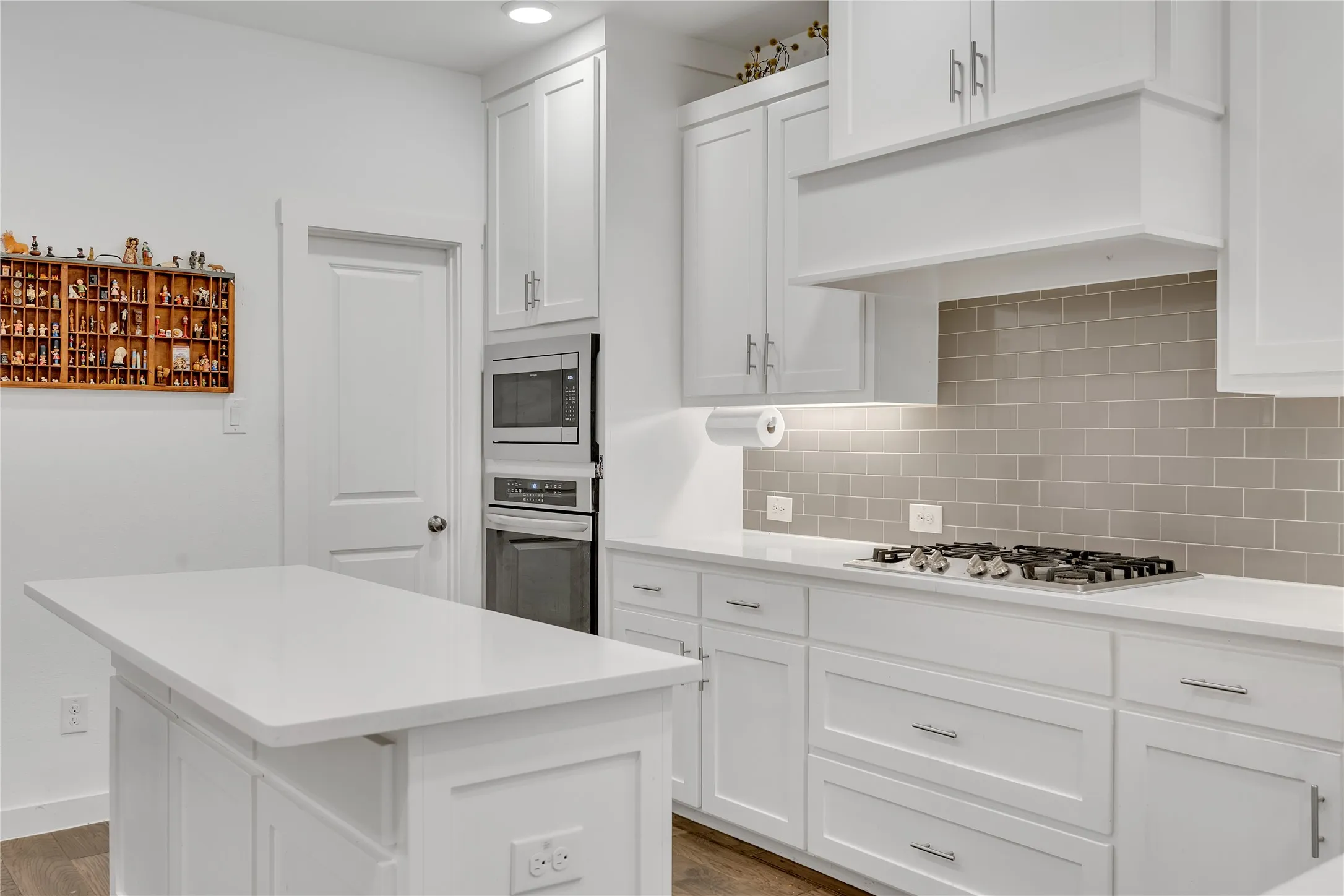 White cabinetry, light-toned subway tile backsplash, white countertops, built-in microwave, and a gas cooktop
