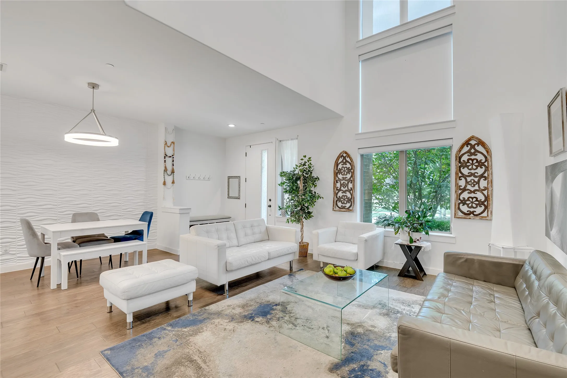 Expansive living area with high ceilings, large windows, wood-finish flooring, a contemporary chandelier, and a textured accent wall