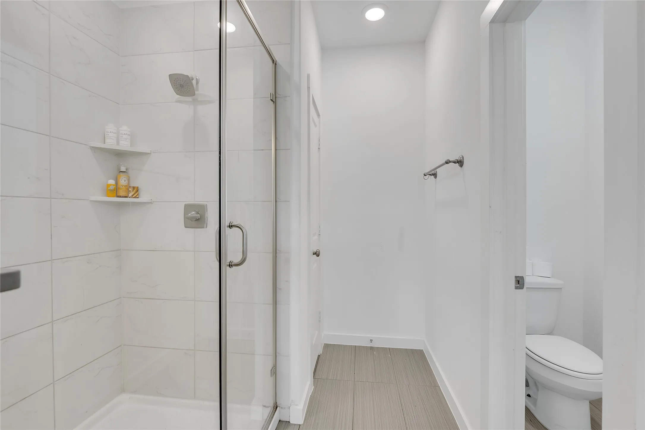 Glass-enclosed shower with tile surround and built-in shelving, complemented by recessed lighting and a towel bar