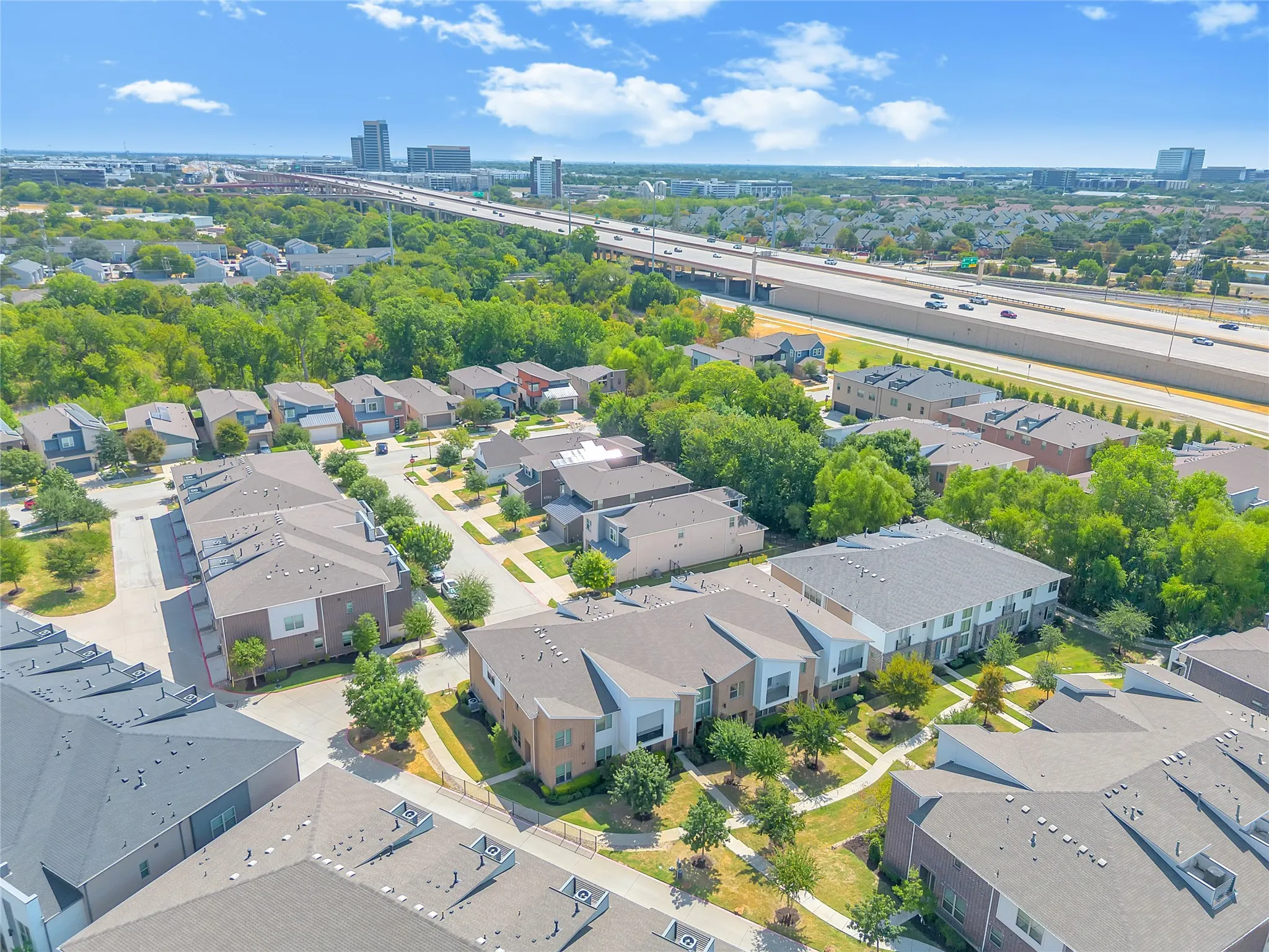 Modern residential development with varied architectural styles, dense surrounding tree canopy, and proximity to major roadways