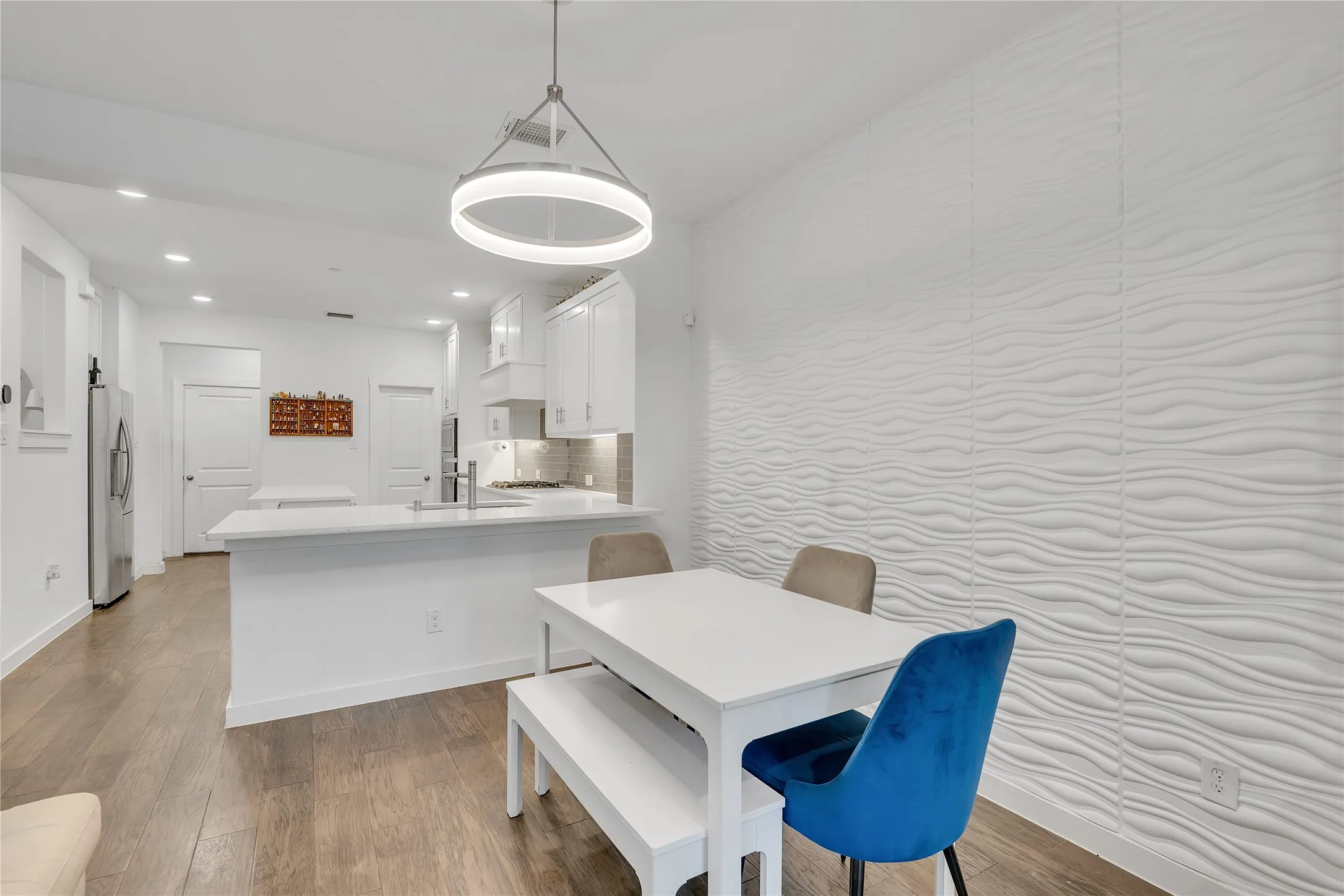 Open-concept dining area with wood-finish flooring, a contemporary circular pendant light, and a textured accent wall