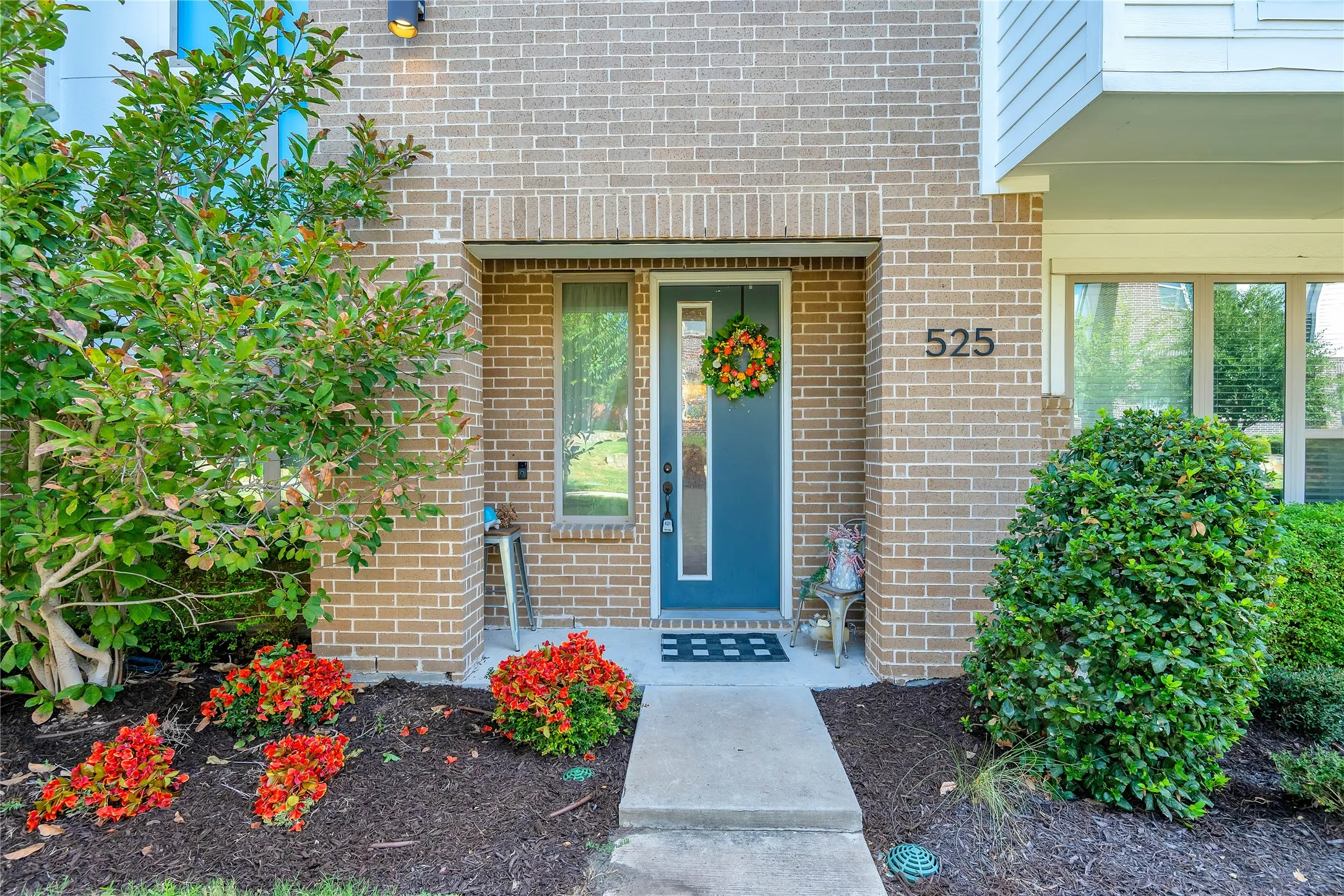 Brick exterior with a prominent entry, modern address numbers, and a landscaped front yard featuring mature shrubs and vibrant red plantings