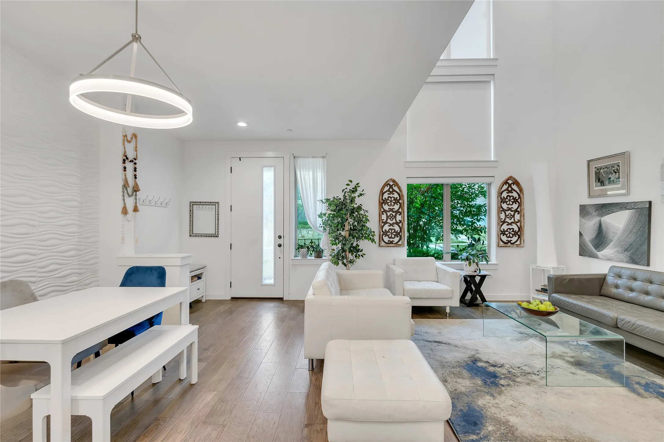 Open-concept living space with wood-finish flooring, soaring ceilings, and a contemporary pendant light fixture