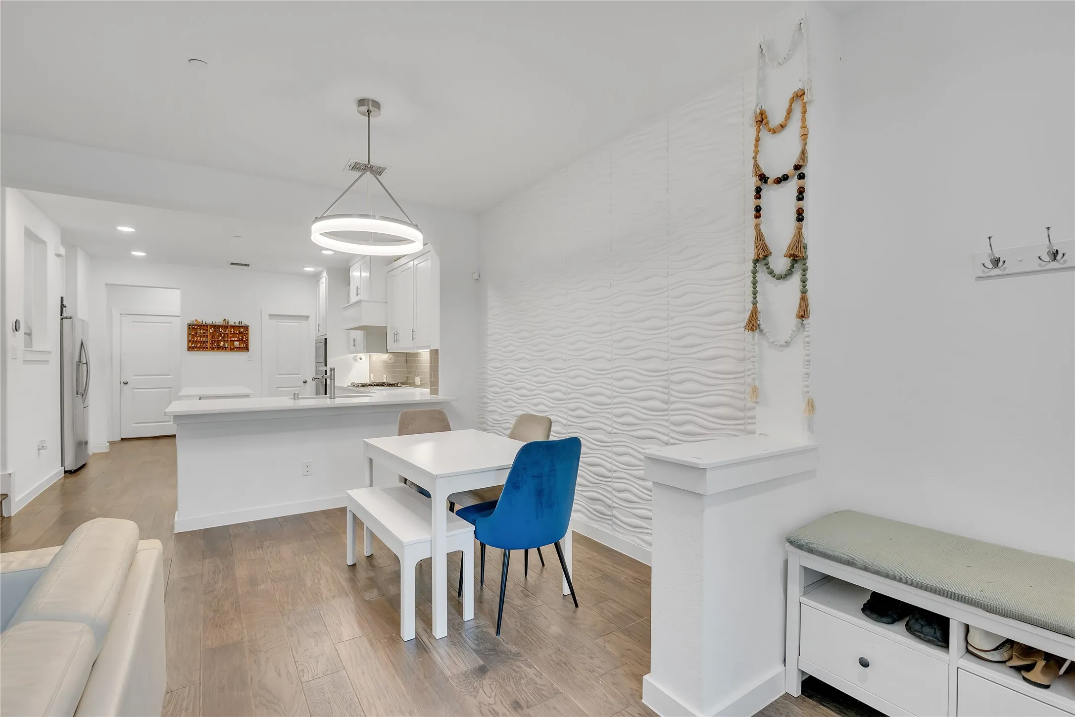 Open-concept living space featuring wood-finish flooring, a contemporary circular pendant light, and a textured accent wall