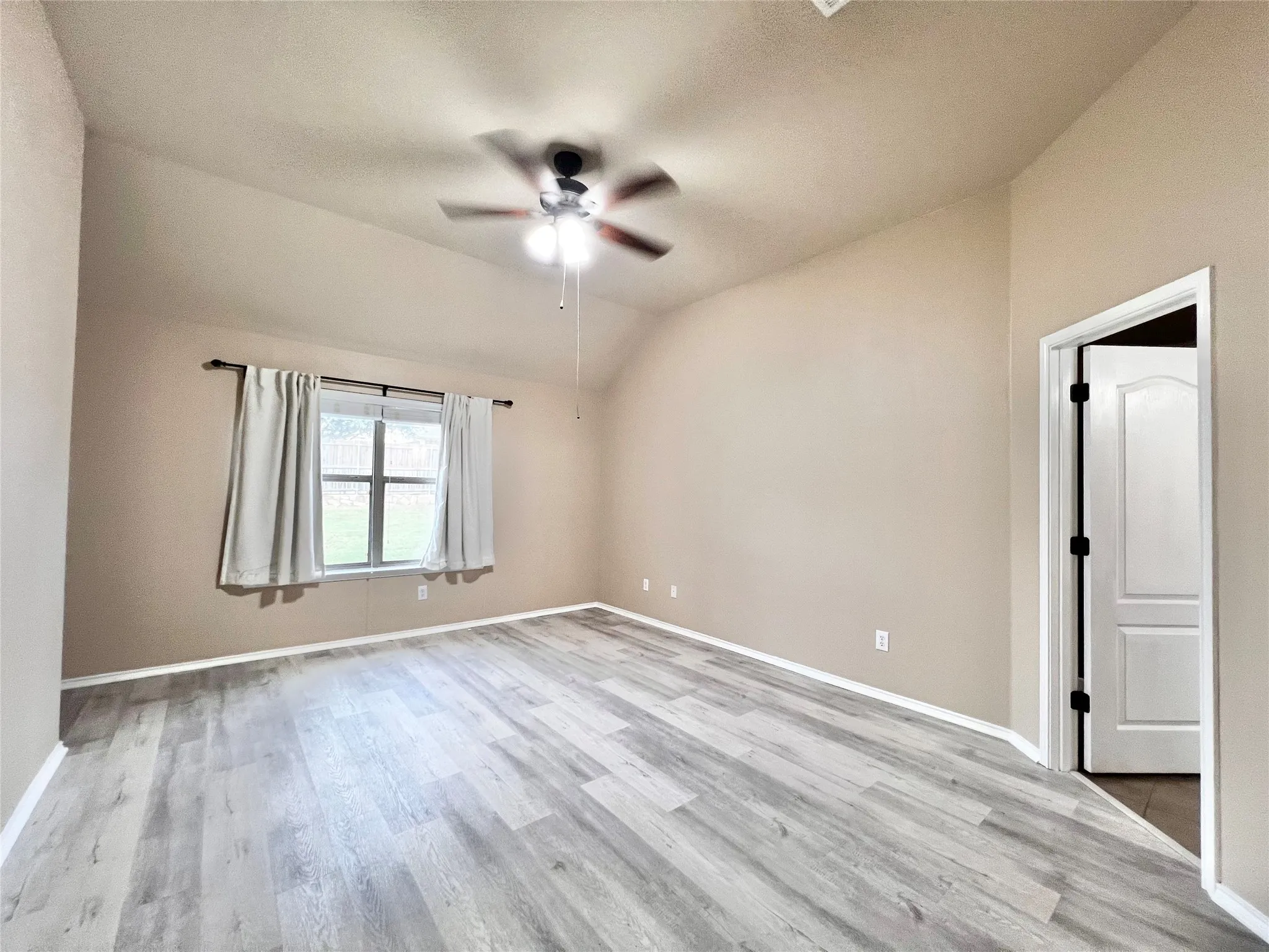 Vaulted ceiling with a ceiling fan, wood-finish flooring, and a multi-pane window