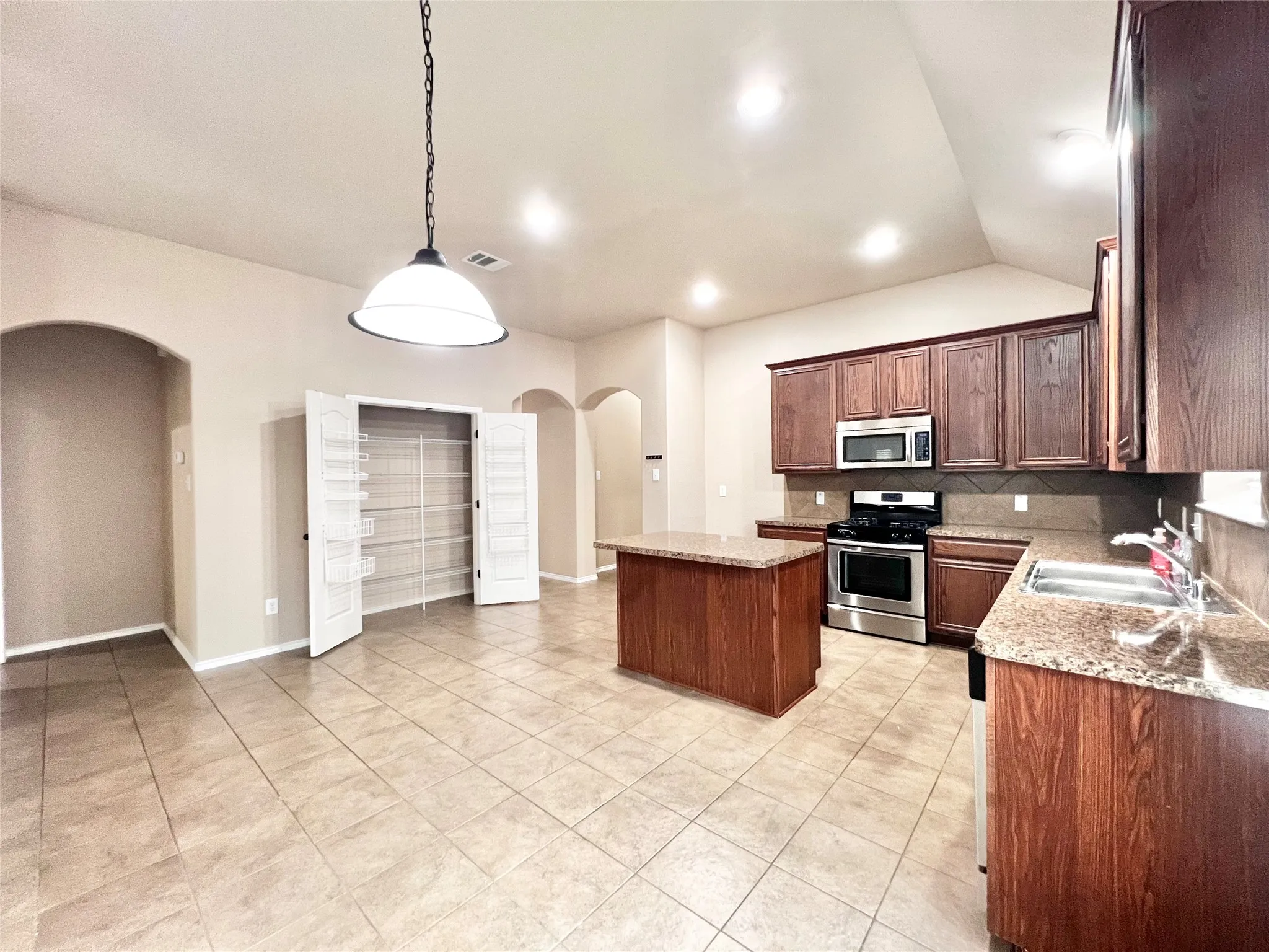 Spacious kitchen featuring a central island, wood cabinetry, stainless steel appliances, and tile flooring