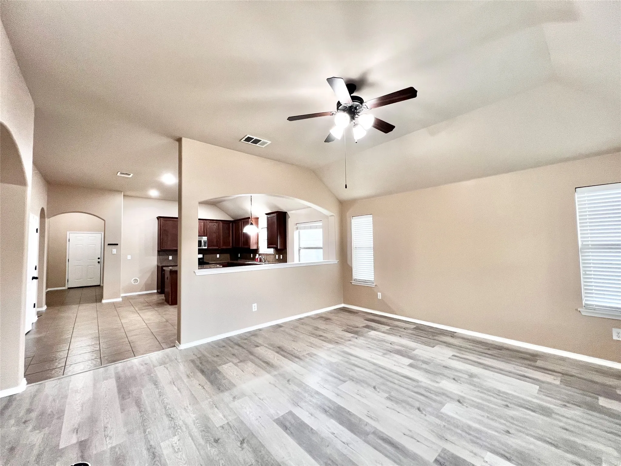 Vaulted ceilings with a ceiling fan, wood-finish flooring, multiple windows with blinds, and an arched entryway