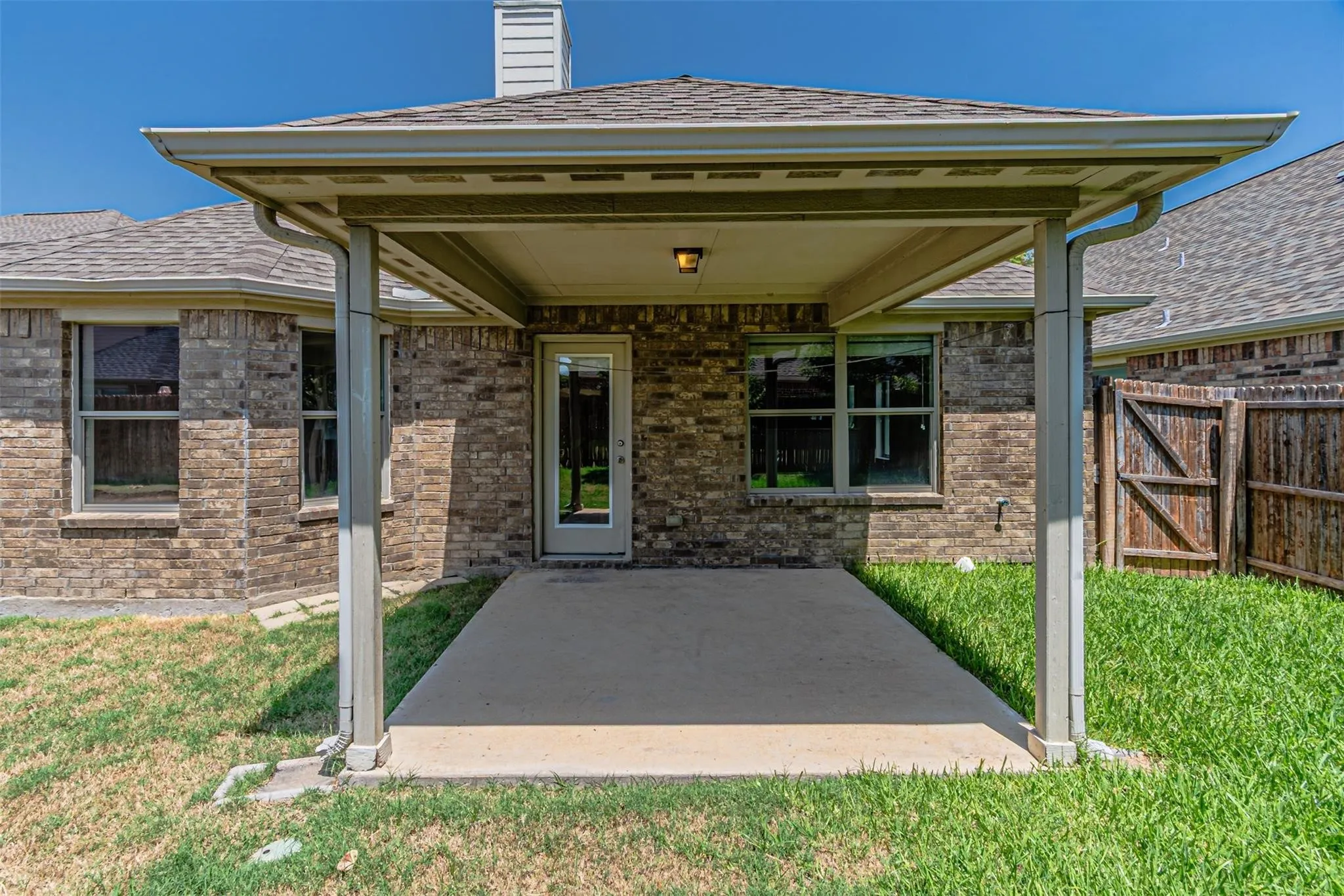 Covered patio with a concrete surface, brick exterior, and a glass-paneled door