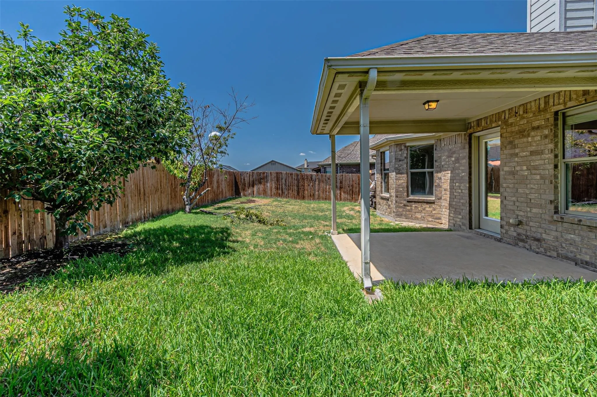 Expansive backyard featuring a covered patio, brick exterior, and a privacy fence