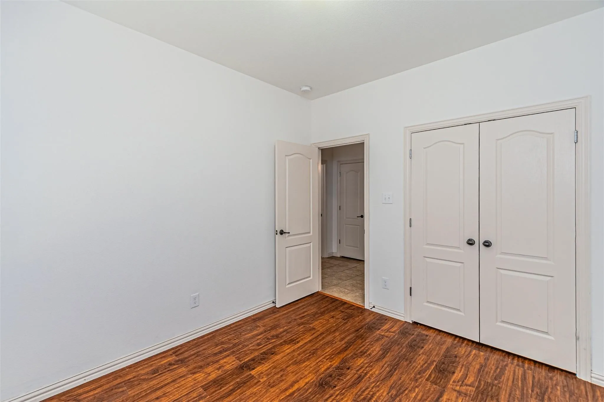 Wood-finish flooring with white baseboards, white walls, and a bi-fold closet with arched panel doors