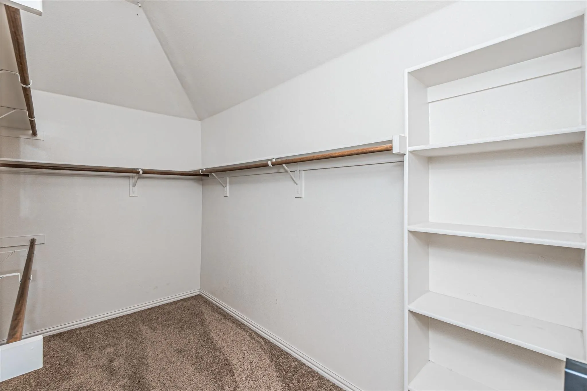 Sloped ceiling design, built-in shelving, hanging rods, and carpet flooring