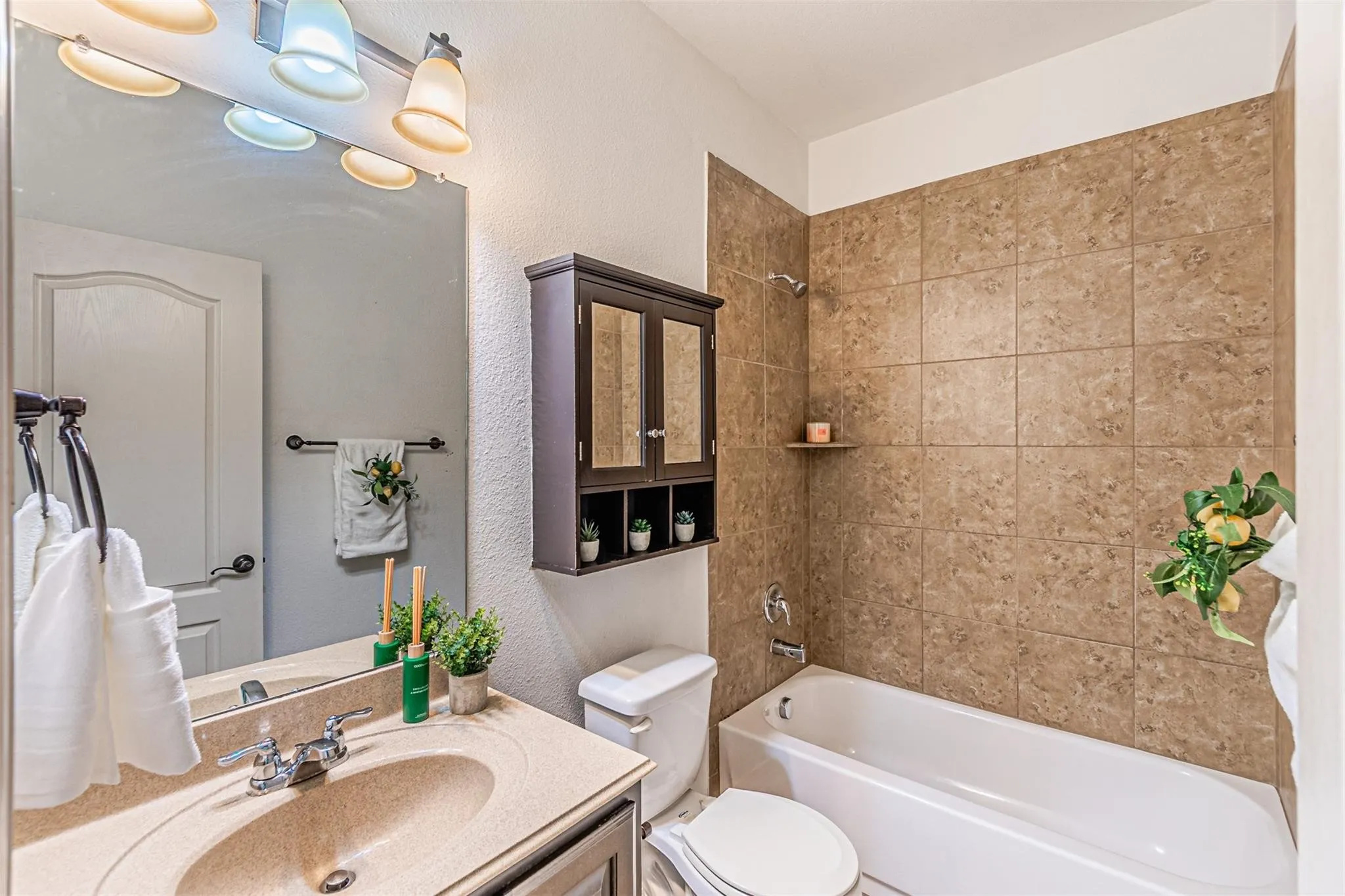 Built-in bathtub with shower, tiled surround, vanity with integrated sink, and wall-mounted medicine cabinet