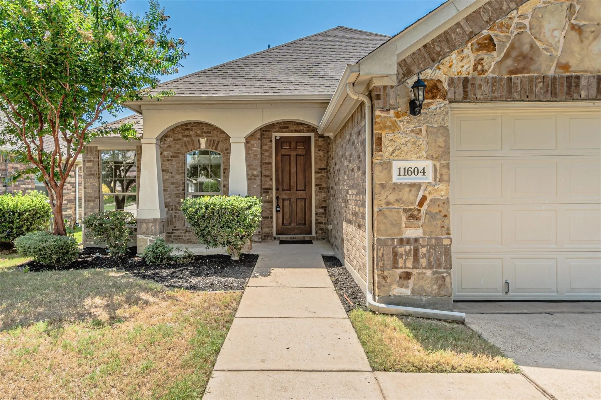 Brick and stone exterior featuring an arched entryway, wood-paneled front door, and an attached garage