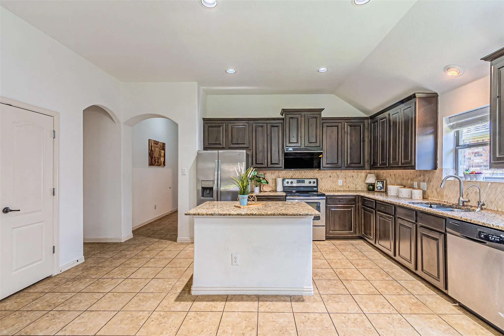 Spacious kitchen featuring an island, dark wood-finish cabinetry, granite countertops, and tile flooring