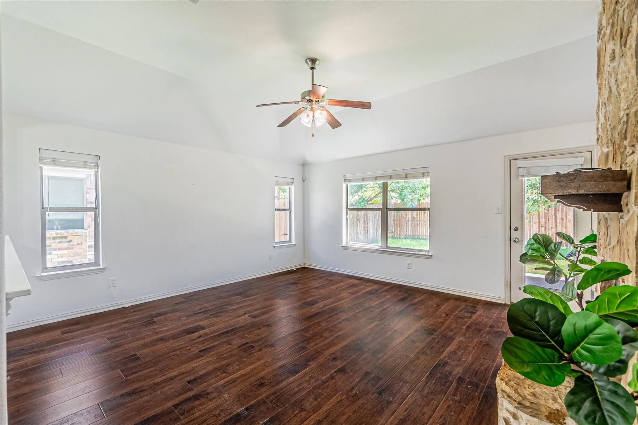 Vaulted ceiling with a ceiling fan, wood-finish flooring, multiple windows, and a stone-clad architectural feature
