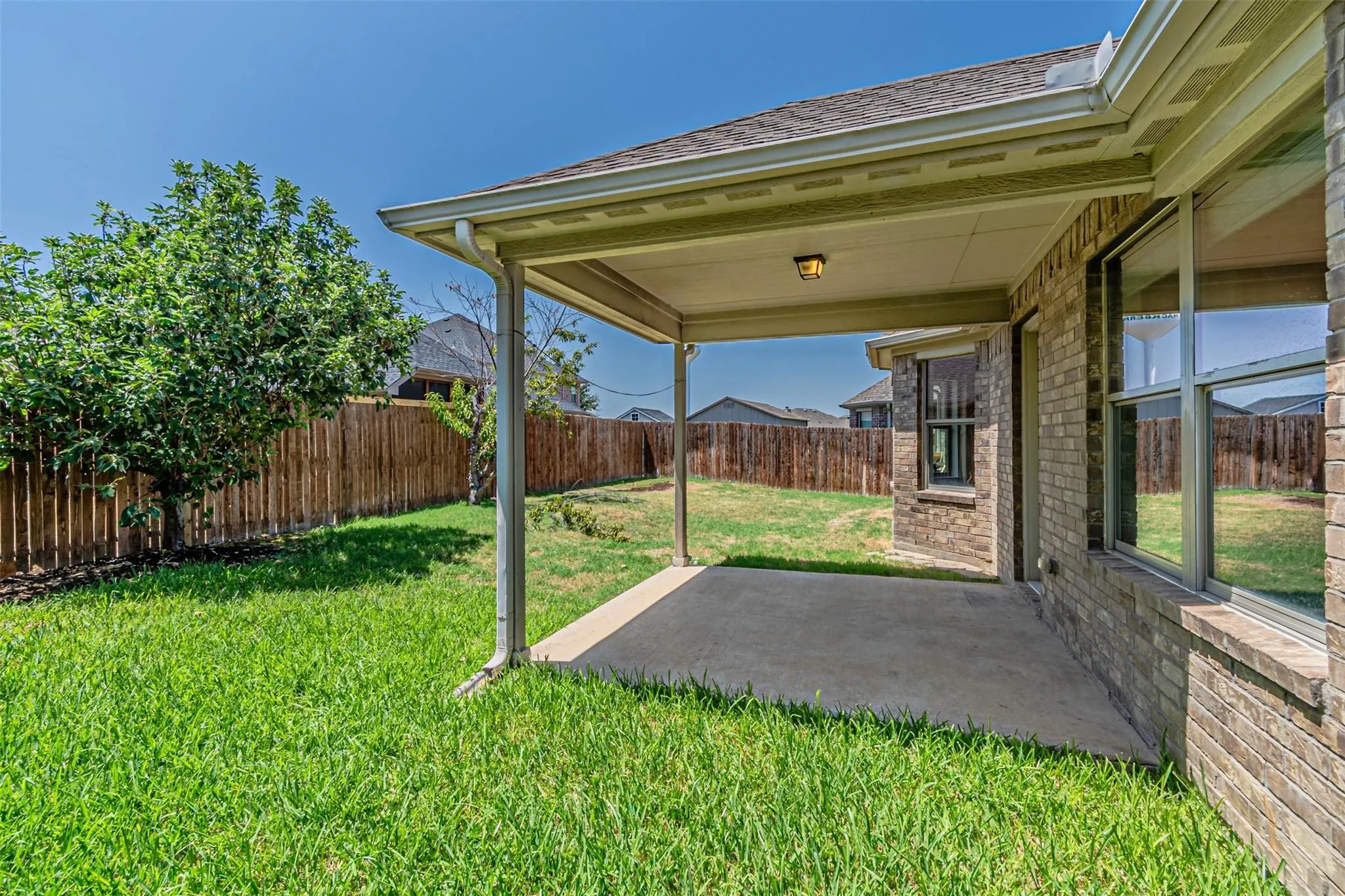 Covered patio with a concrete slab, brick exterior, and a fenced backyard featuring a tree
