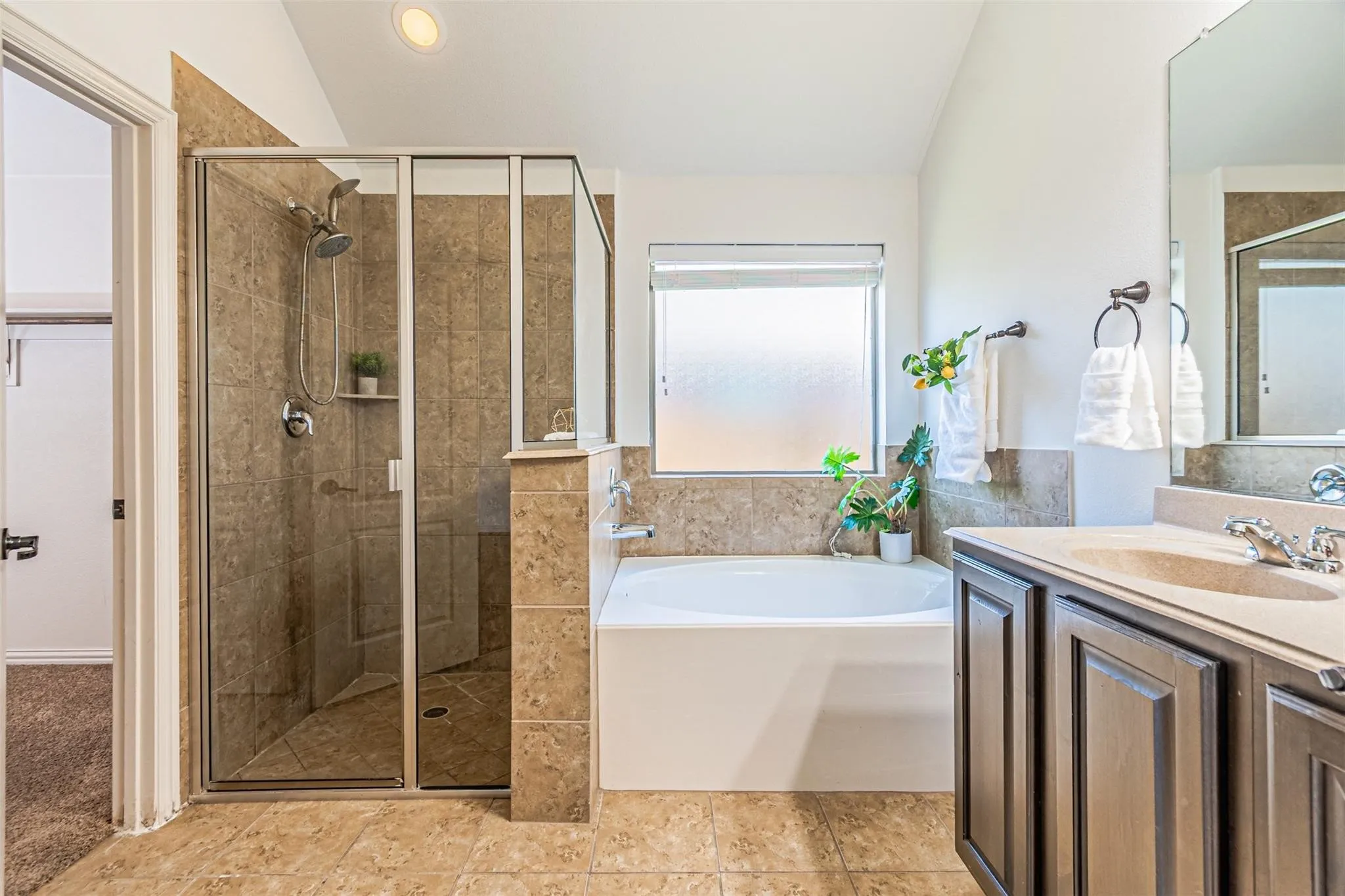 Expansive tile flooring, separate shower with glass enclosure, built-in bathtub, and a double vanity with an integrated sink