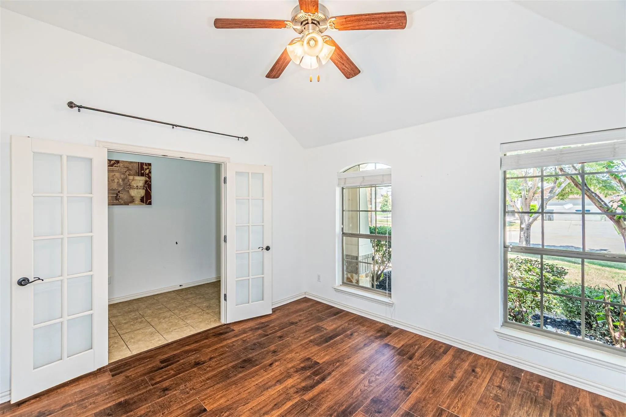 Vaulted ceiling with a ceiling fan, wood-finish flooring, two large windows, an arched window, and double French doors