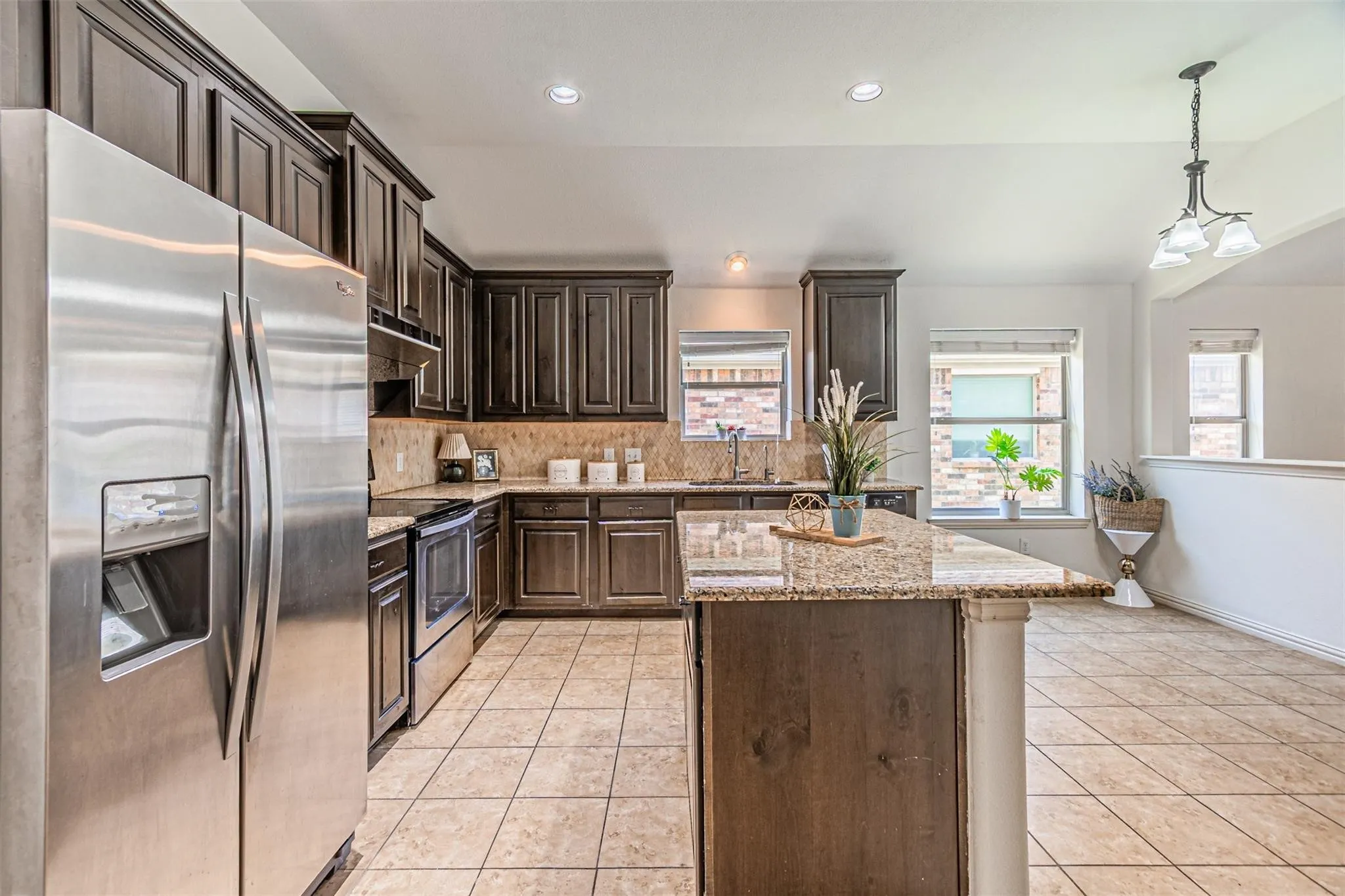 Kitchen featuring dark wood cabinetry, stainless steel appliances, granite countertops, a center island, and tile flooring