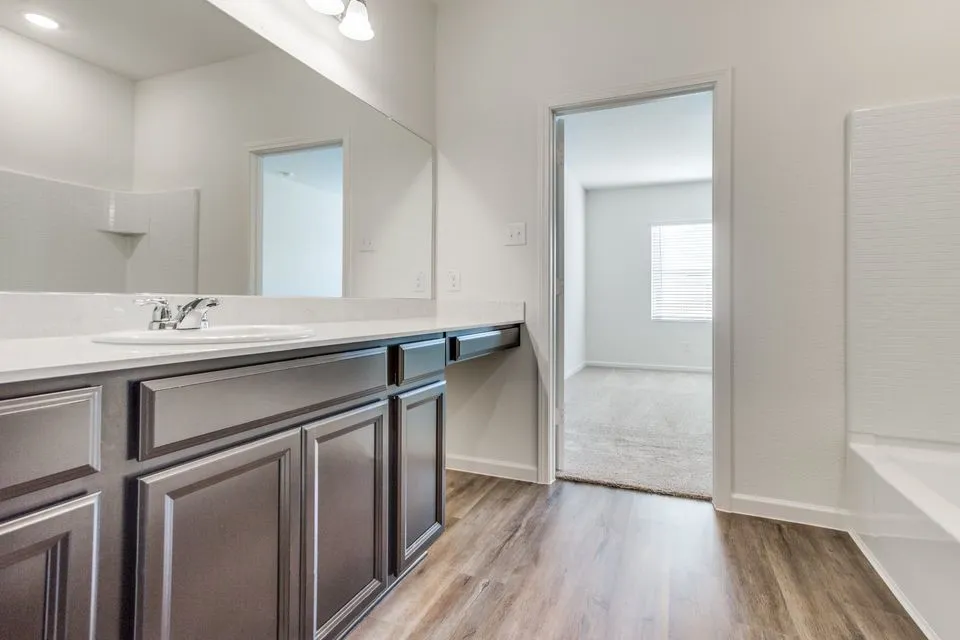 Wood-finish flooring, vanity with integrated sink, expansive vanity mirror, light-toned countertop, and recessed lighting