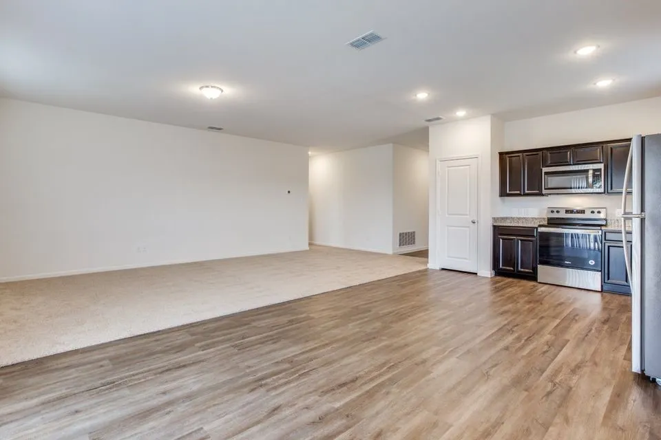 Open-concept living space with wood-finish flooring, recessed lighting, and a kitchen featuring dark cabinetry, stainless steel appliances, and a light-toned countertop