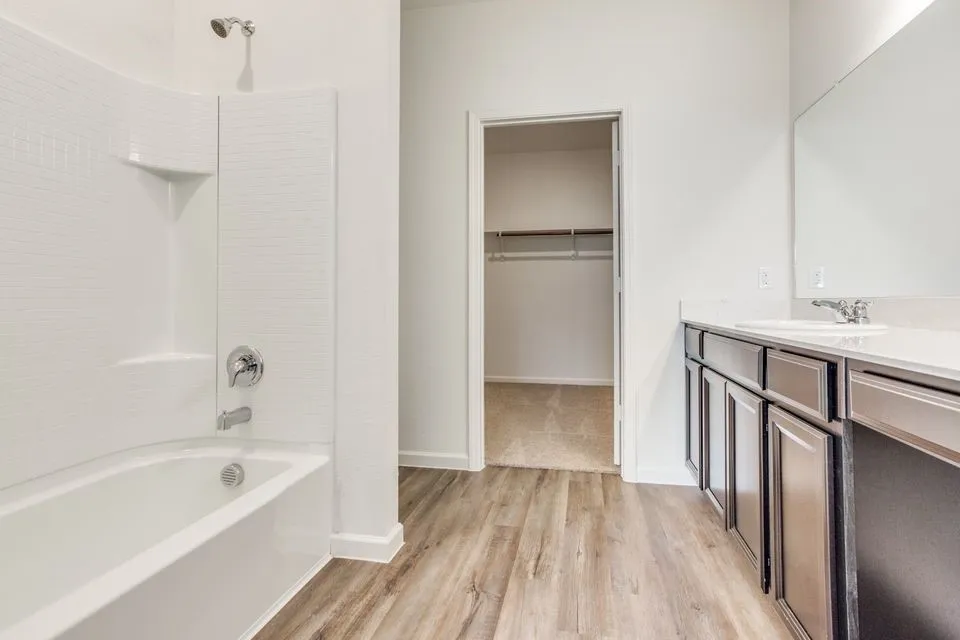 Tub and shower combination with white subway tile surround, wood-finish flooring, dark wood-finish vanity with countertop, and large wall-mounted mirror