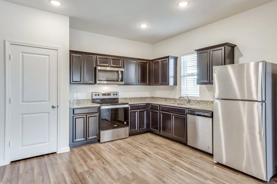 Kitchen featuring dark wood cabinetry, stainless steel appliances, granite-style countertops, wood-finish flooring, and recessed lighting
