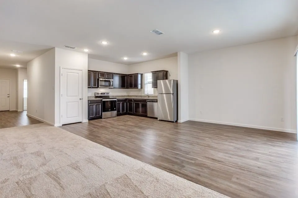 Open-concept living area featuring wood-finish flooring, recessed lighting, and a kitchen with dark cabinetry and stainless steel appliances