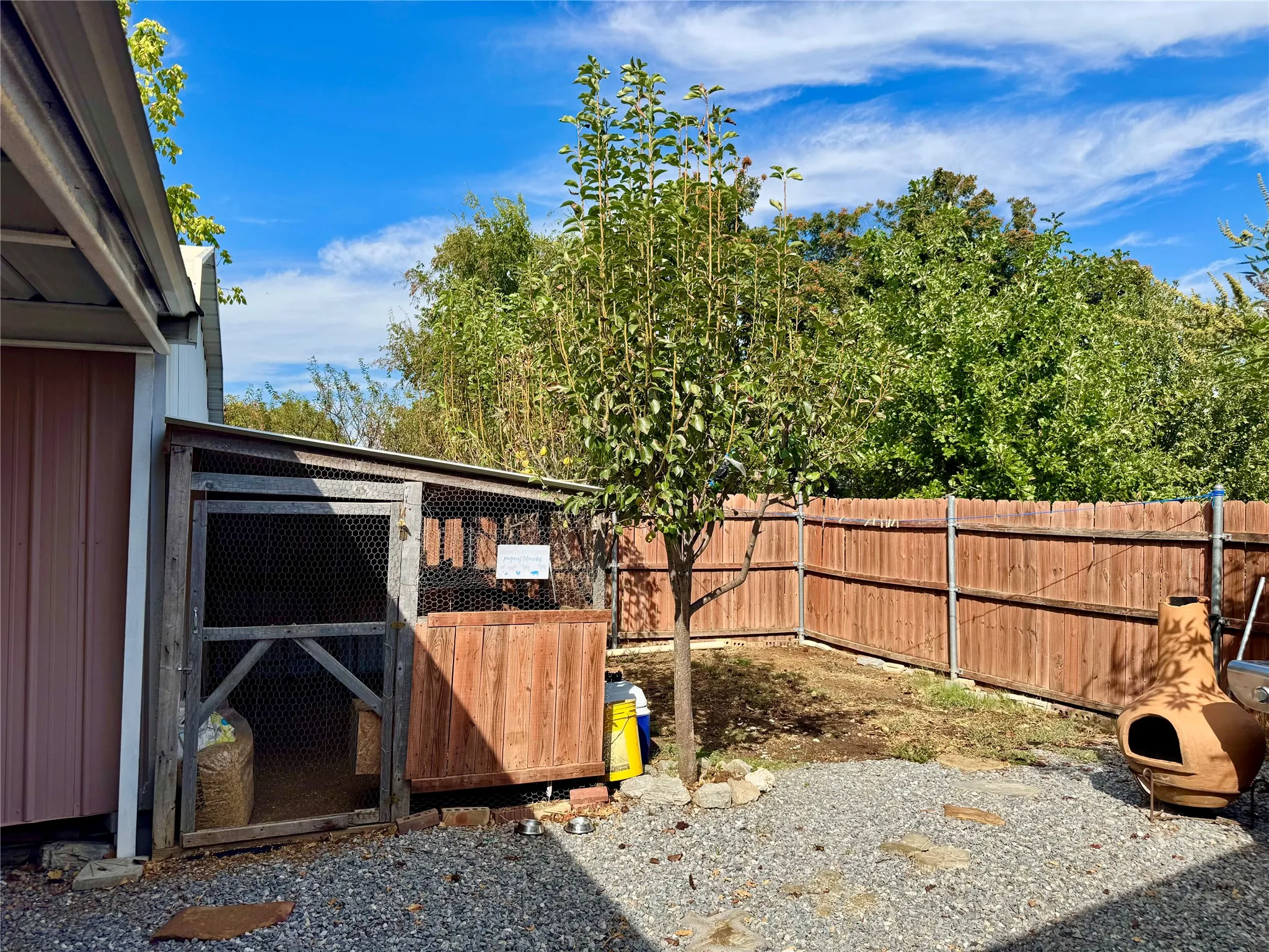 Partial fenced backyard with chicken coop, fruit tree, gravel pathways