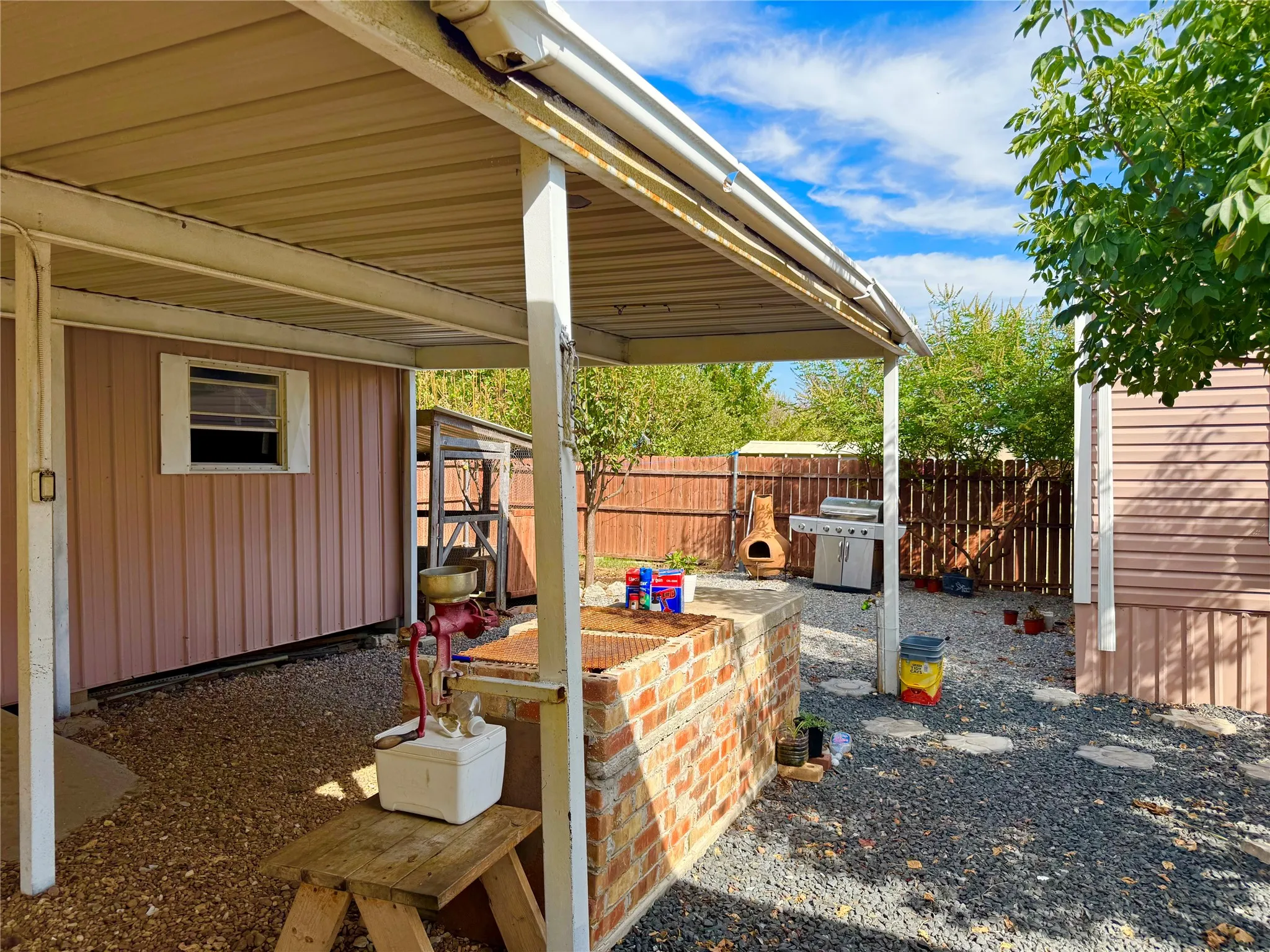 Gravel patio area featuring a covered awning, brick outdoor counter, and wood fencing