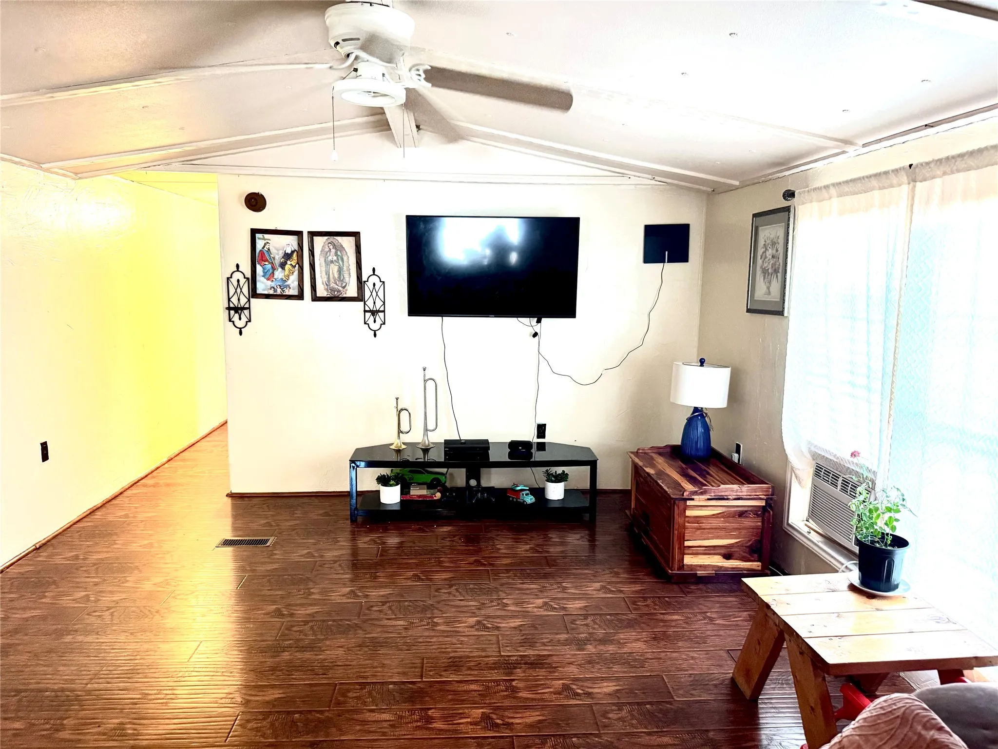 Laminate wood-finish flooring throughout, ceiling fan with integrated lighting, and a large window with sheers