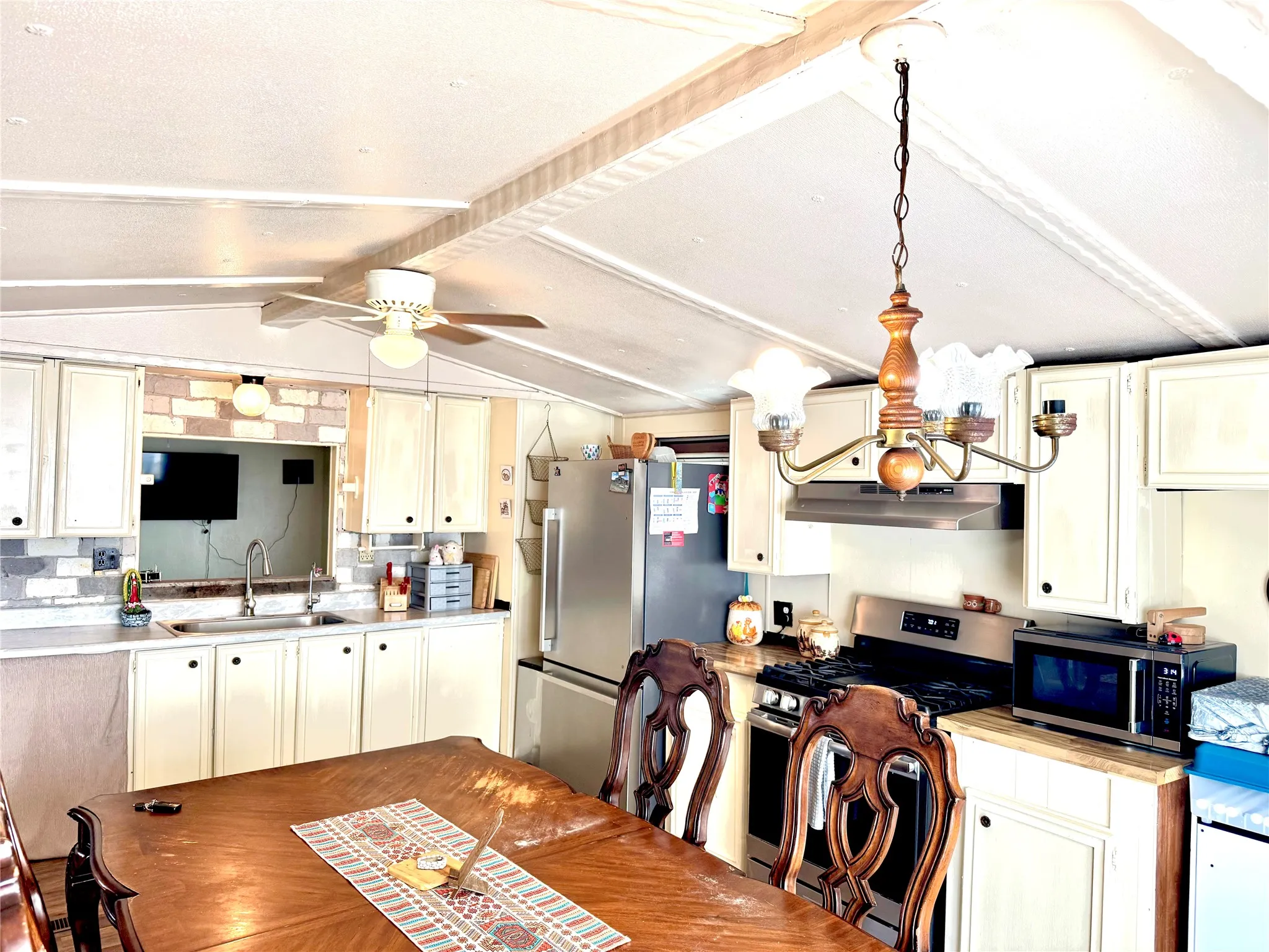 Kitchen featuring white cabinetry, stainless steel appliances, a ceiling fan, and a wood chandelier