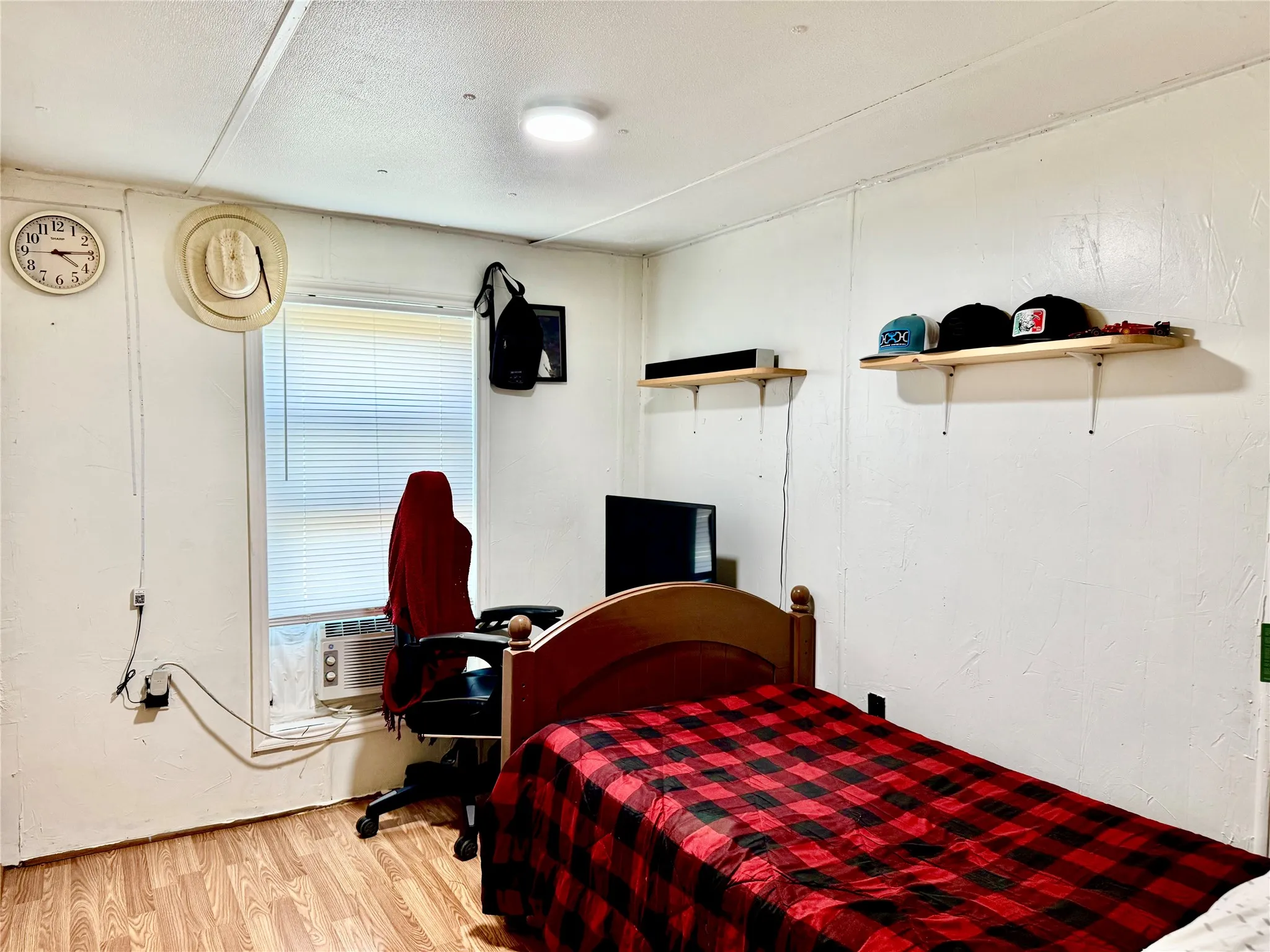 Window with blinds, overhead flush-mount lighting, and wall-mounted shelving