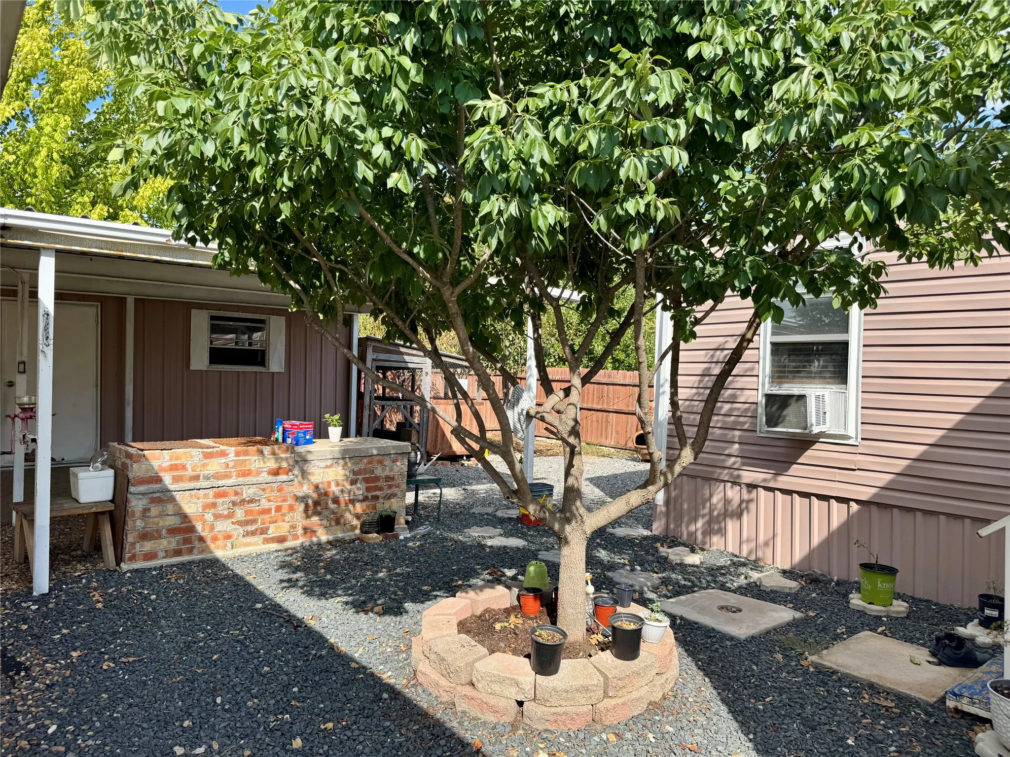 Gravel-covered outdoor space featuring a mature tree with a stone-lined base