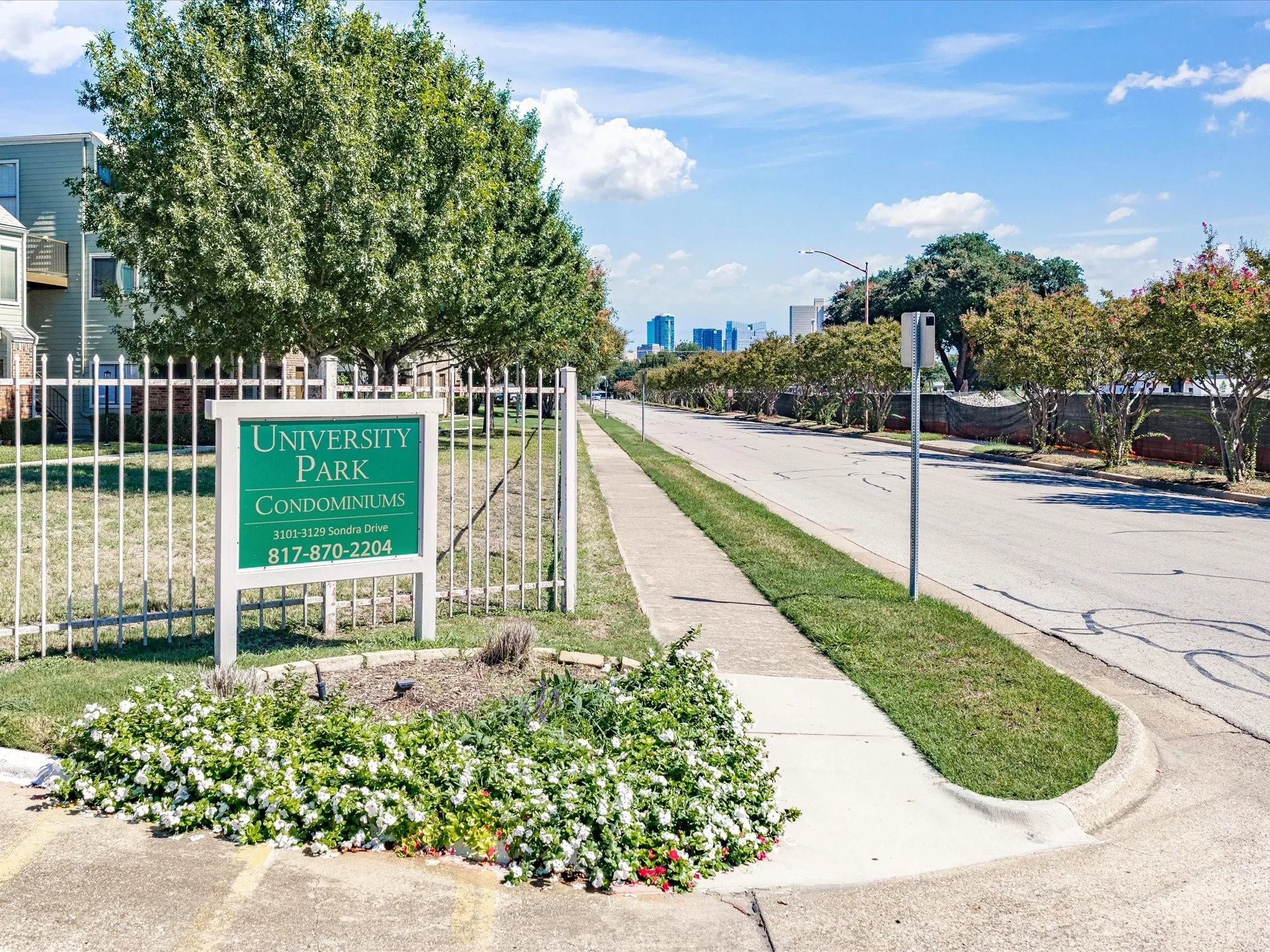 University Park Condominiums signage with white fencing, bordered by mature trees and a manicured lawn