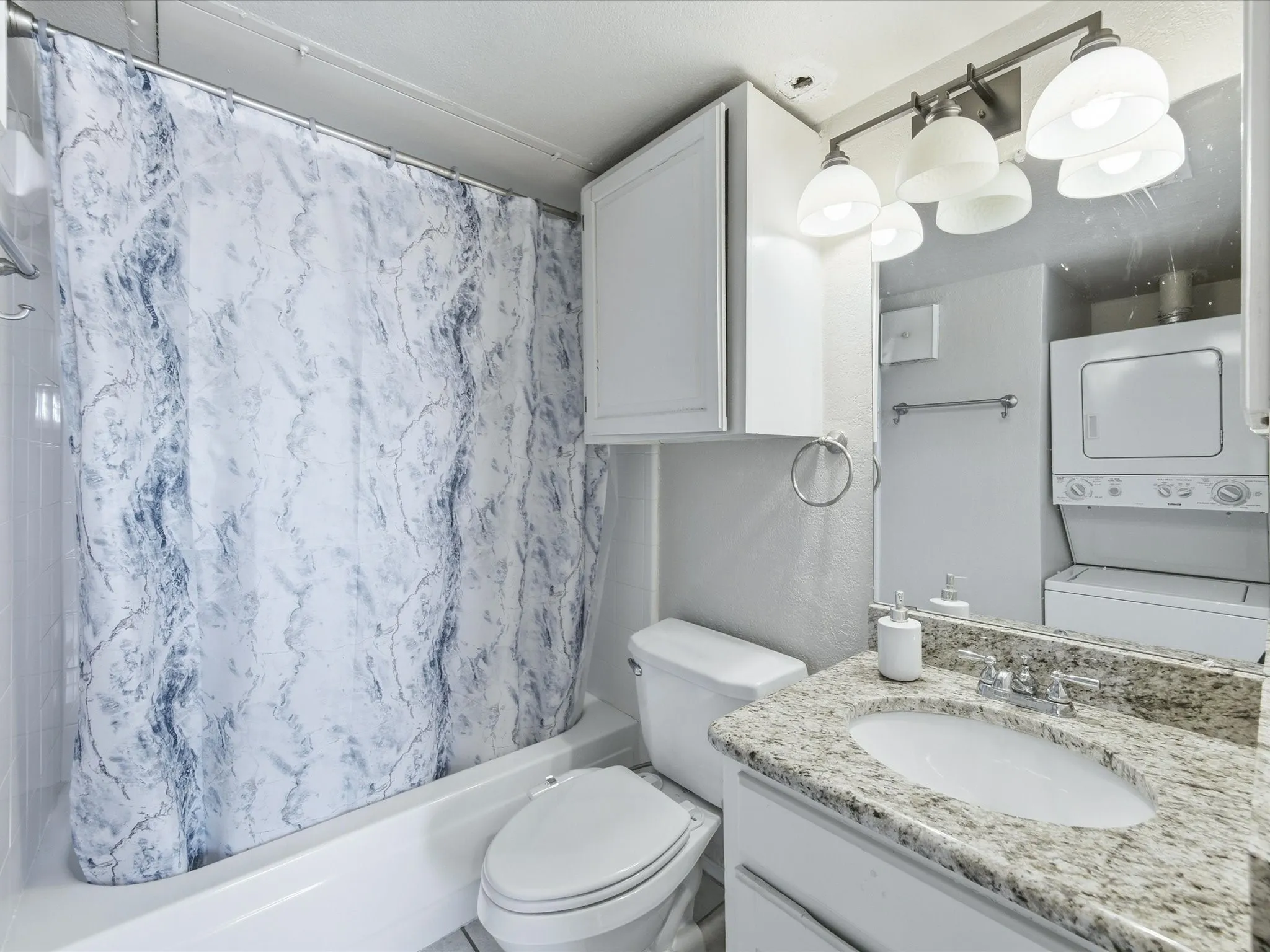 Bathroom featuring a shower-tub combination, a toilet, a vanity with a granite countertop, and a stacked washer and dryer