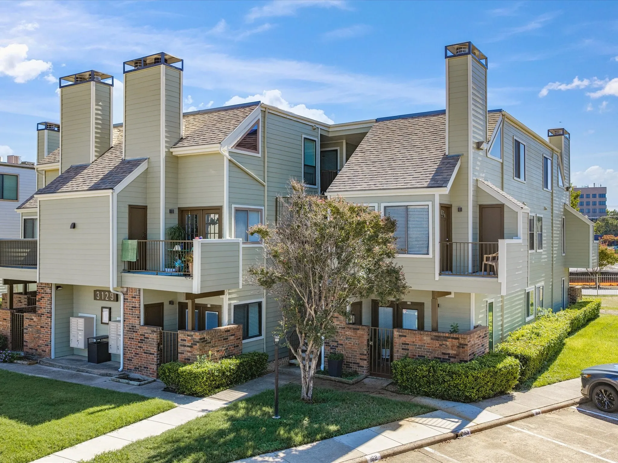 Contemporary townhome community featuring distinctive architectural elements including peaked rooflines, multiple chimney stacks, and mixed exterior finishes in light-colored siding and brick