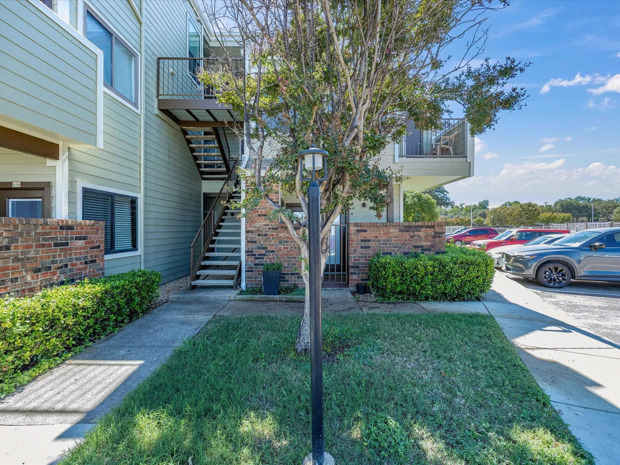 Exterior siding in a light green finish, brick accent wall, and a multi-level structure with an upper balcony featuring a metal railing