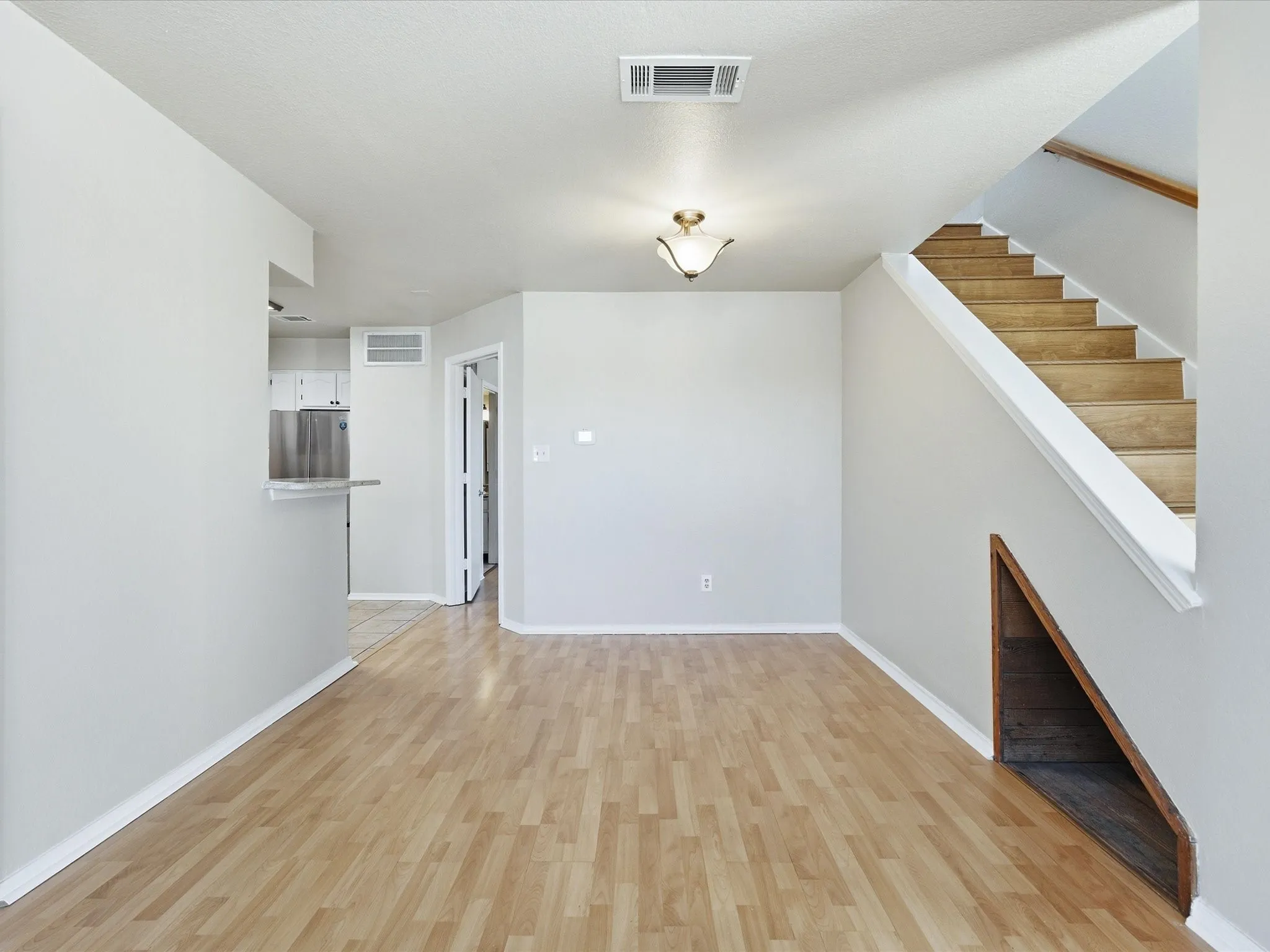 Wood-finish flooring throughout, staircase with wood treads and white risers, under-stair storage nook, and ceiling-mounted light fixture