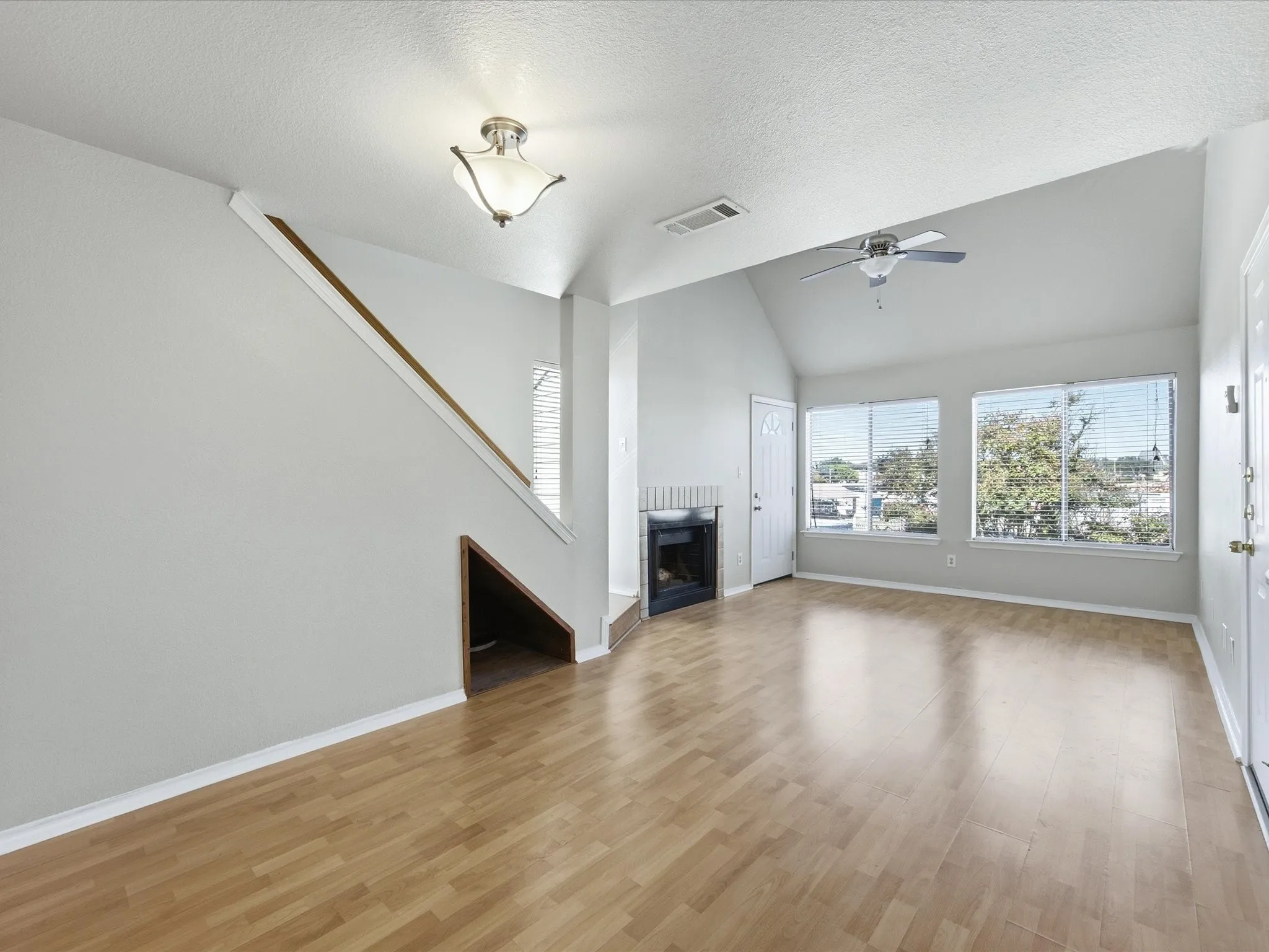 Vaulted ceiling, wood-finish flooring, multiple windows with blinds, built-in fireplace, and a ceiling fan