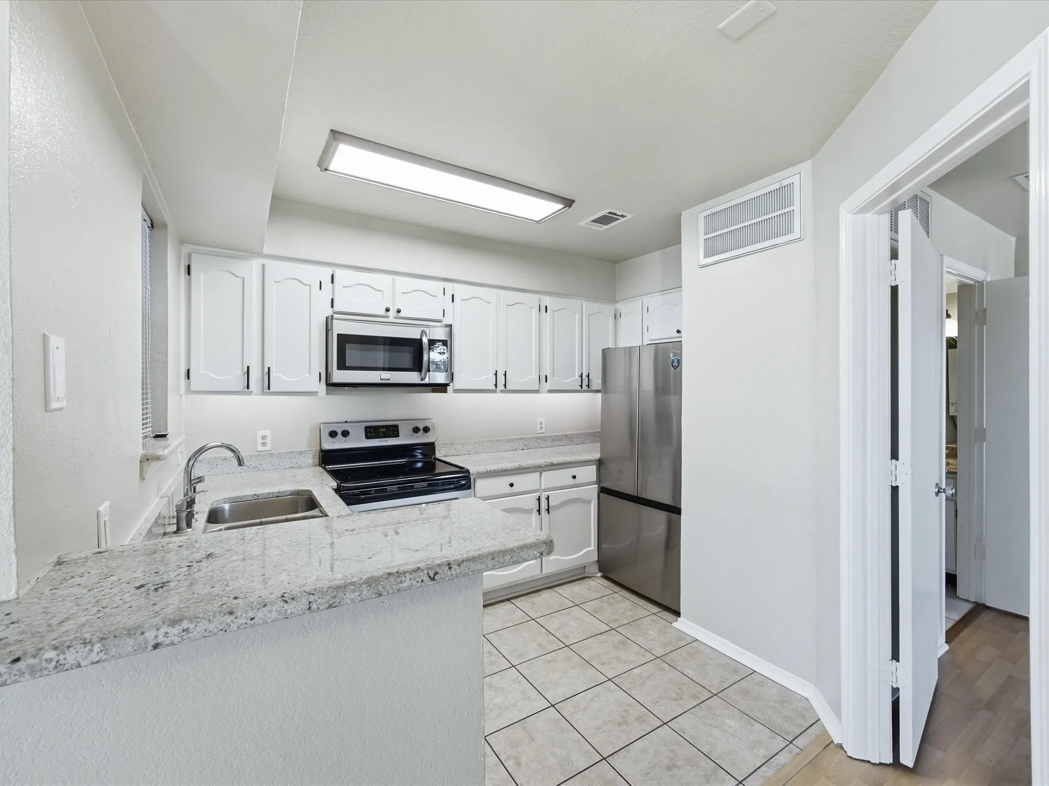 White cabinetry, stainless steel appliances, tile flooring, light-toned countertops, and recessed lighting