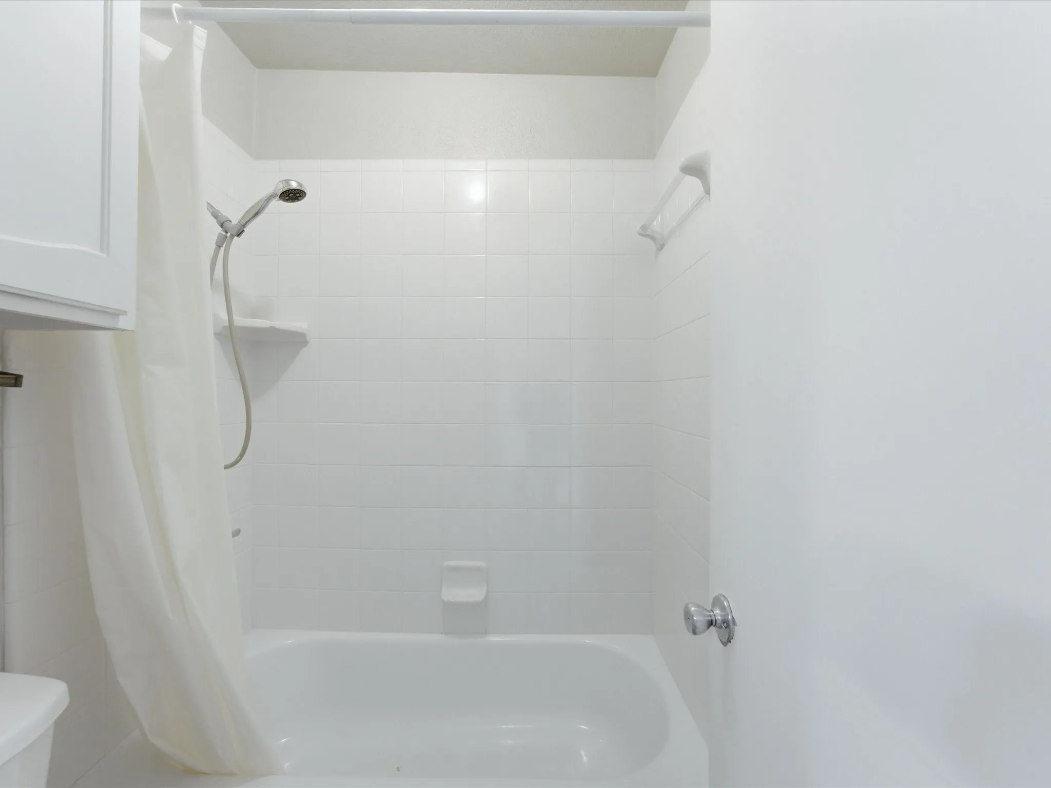 Bathtub with white tile surround, integrated showerhead, and wall-mounted soap dish