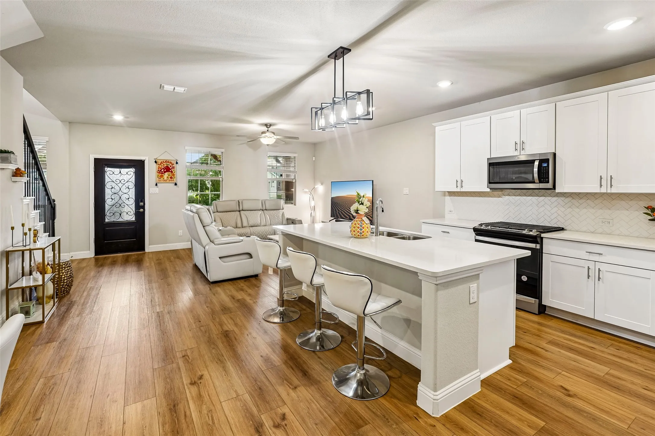 Open-concept living area featuring wood-finish flooring, a kitchen island with seating, a stainless steel microwave and stove, and white cabinetry