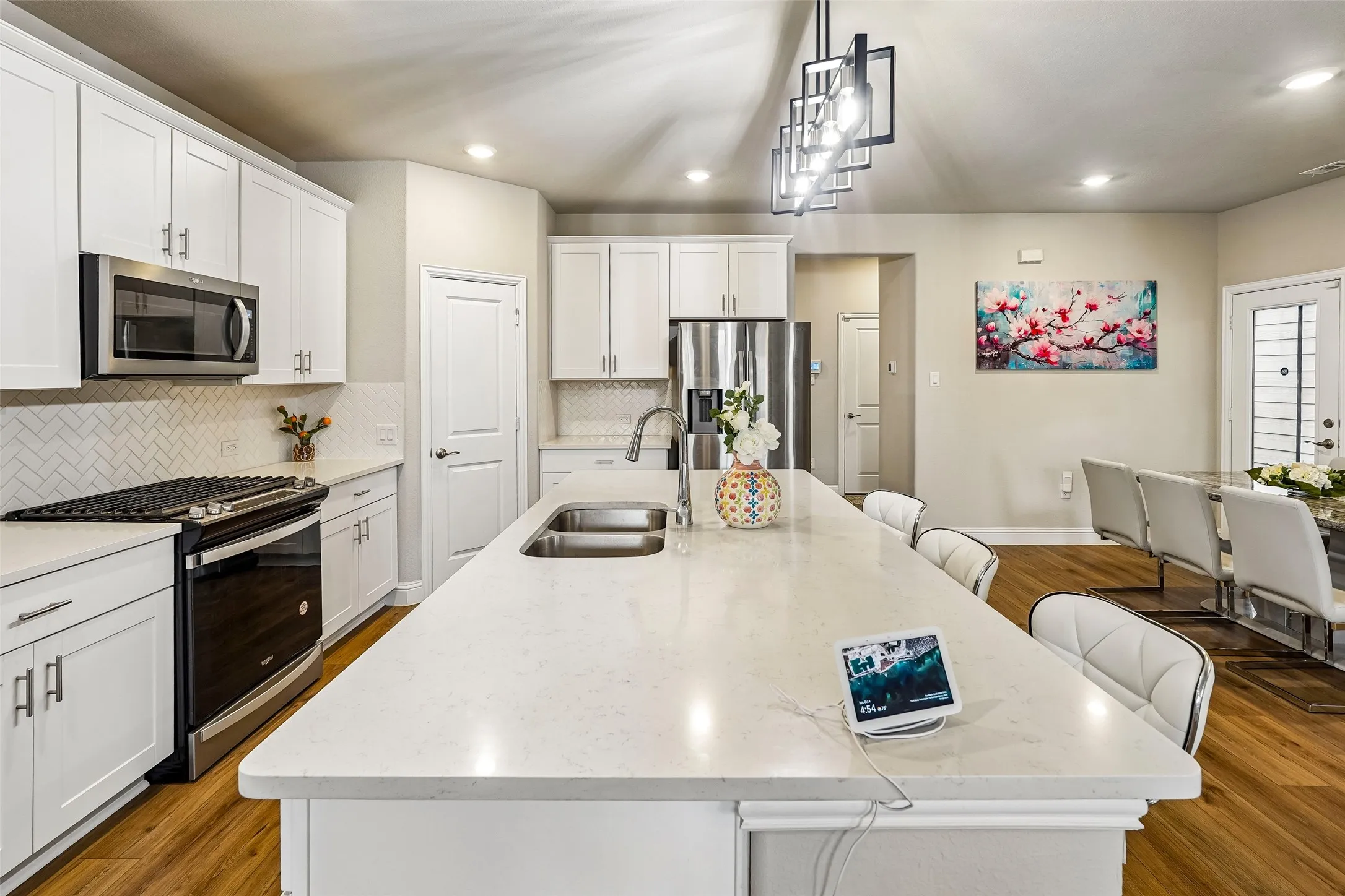 Kitchen featuring white shaker cabinetry, stainless steel appliances, a herringbone tile backsplash, an oversized center island with an integrated double basin sink, and wood-finish flooring