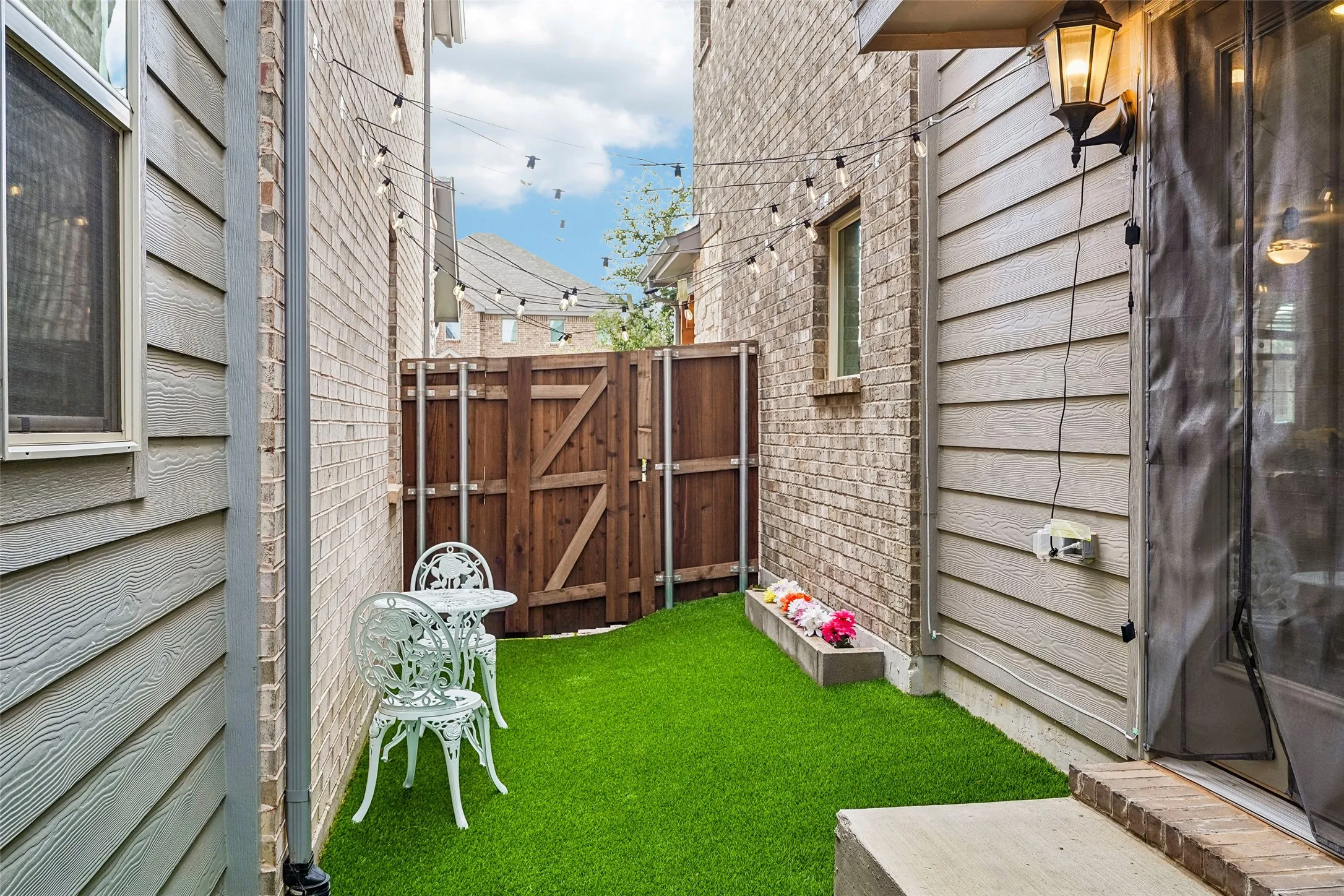 Enclosed outdoor space featuring artificial turf, a privacy fence, and brick and siding exterior finishes